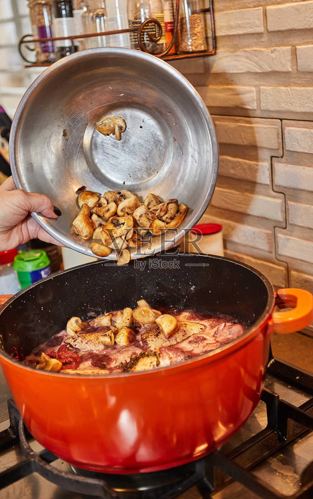 厨师将蘑菇加入到煤气炉上红酒和迷迭香腌制的鸡肉锅中照片摄影图片