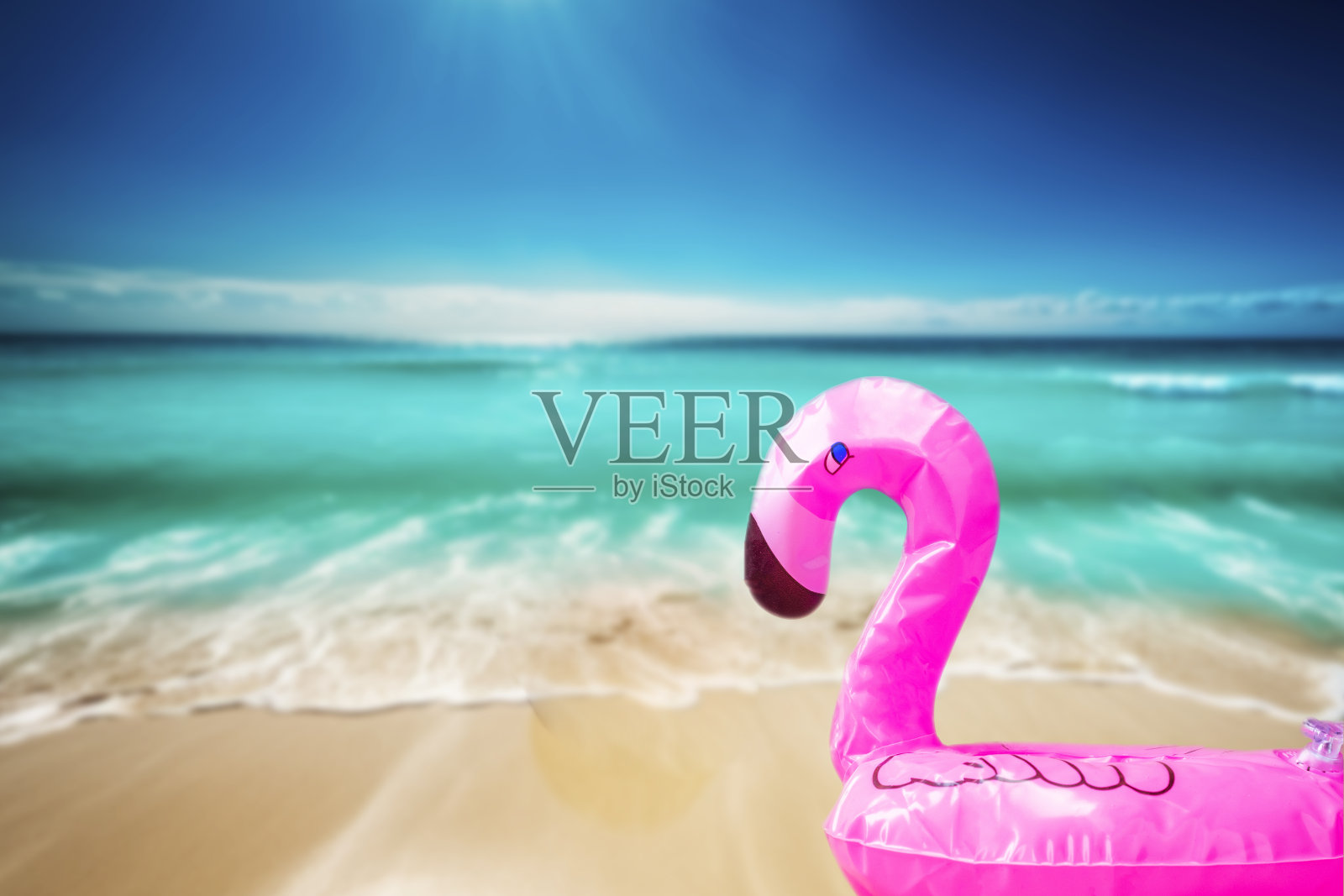 粉红色，时髦，吹海滩火烈鸟在赏金海滩与蓝色的海水背景。打夏天。粉红色的火烈鸟。粉红色火烈鸟，热带鸟类形状充气游泳池。照片摄影图片