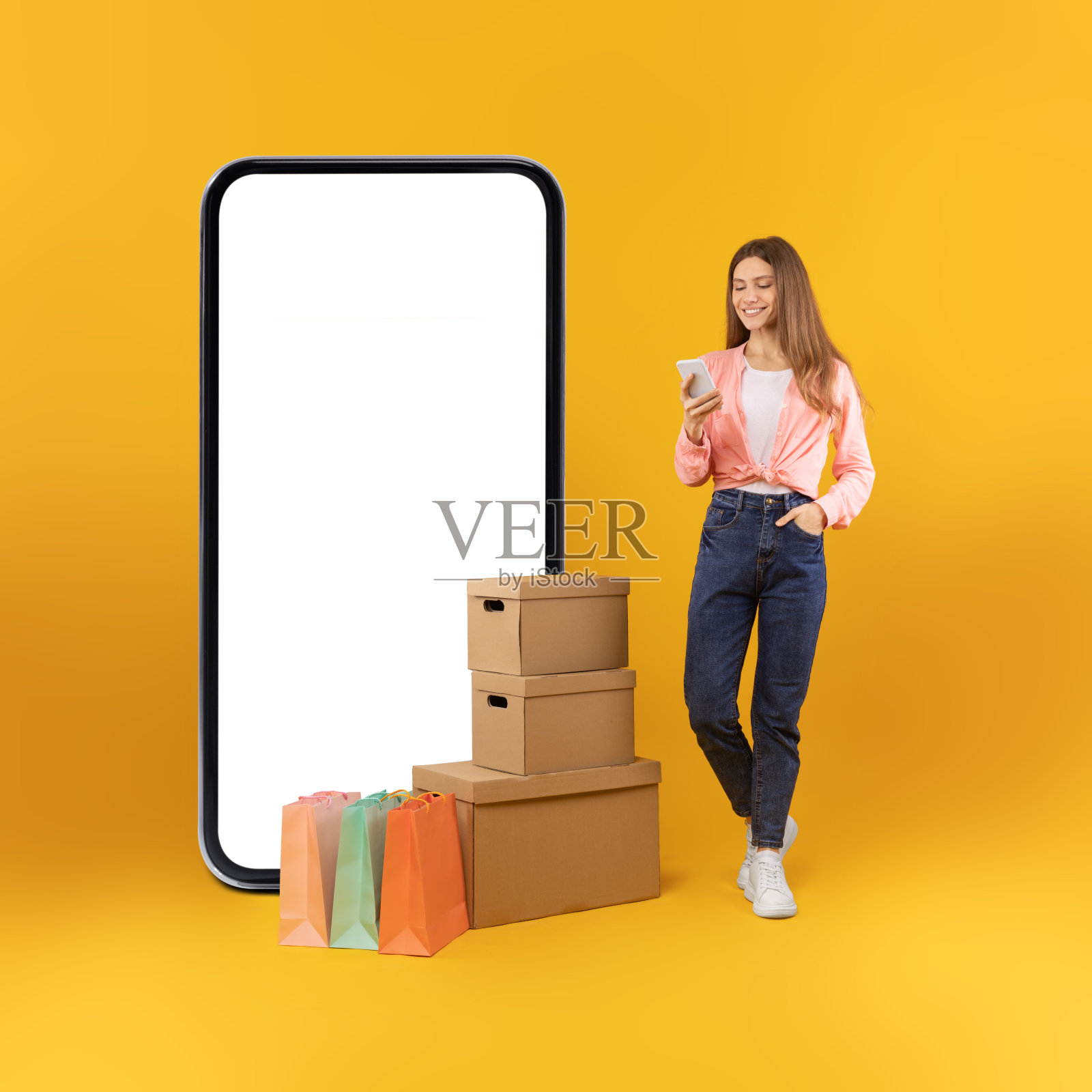 欢快的女买家在黄色背景的大智能手机旁摆姿势照片摄影图片