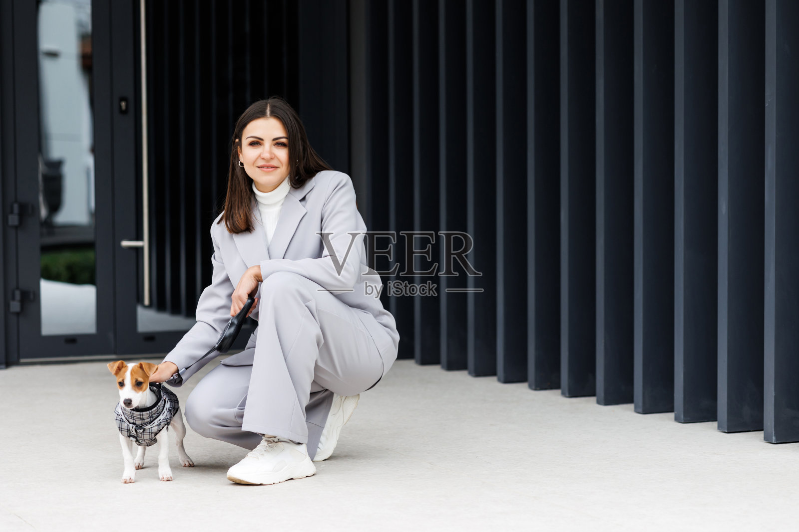 一位穿着休闲夹克的女士坐在她最喜欢的毛绒绒的纯种杰克罗素梗狗旁边，她穿着秋日户外咖啡馆的狗装。照片摄影图片