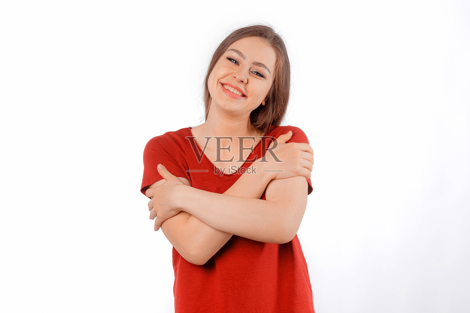 风趣俏皮的年轻女子，长头发，抱着自己，开心地笑着，梦想着找到灵魂伴侣。穿着红色t恤的迷人女模特在白色的工作室背景上摆姿势照片摄影图片