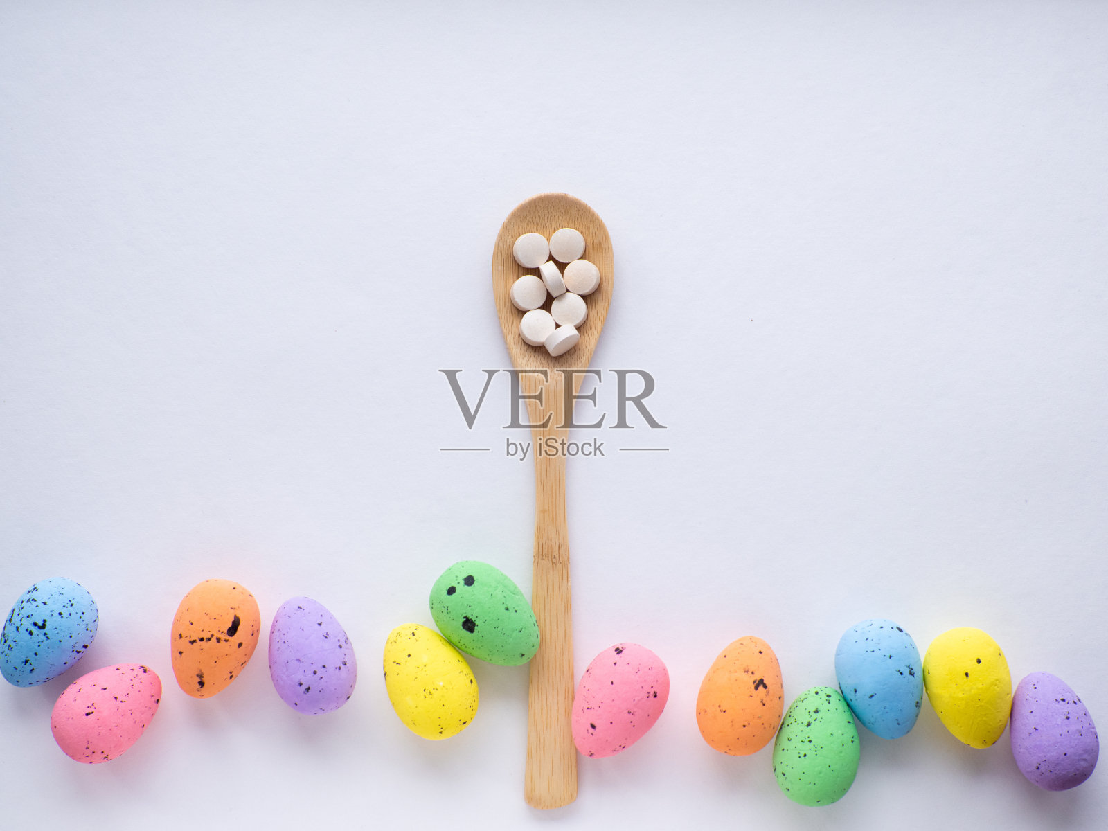 木勺里装着药丸，周围是白色背景上五颜六色的复活节彩蛋照片摄影图片