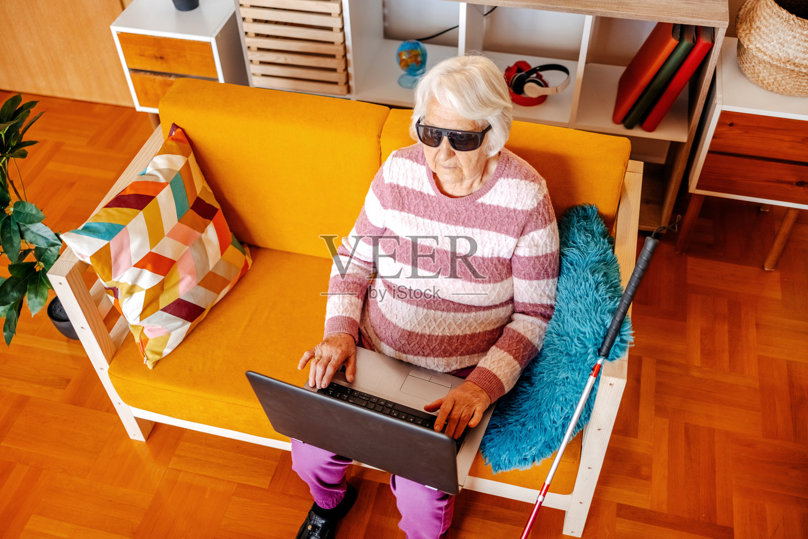 坐在客厅沙发上用笔记本电脑的瞎老太太照片摄影图片