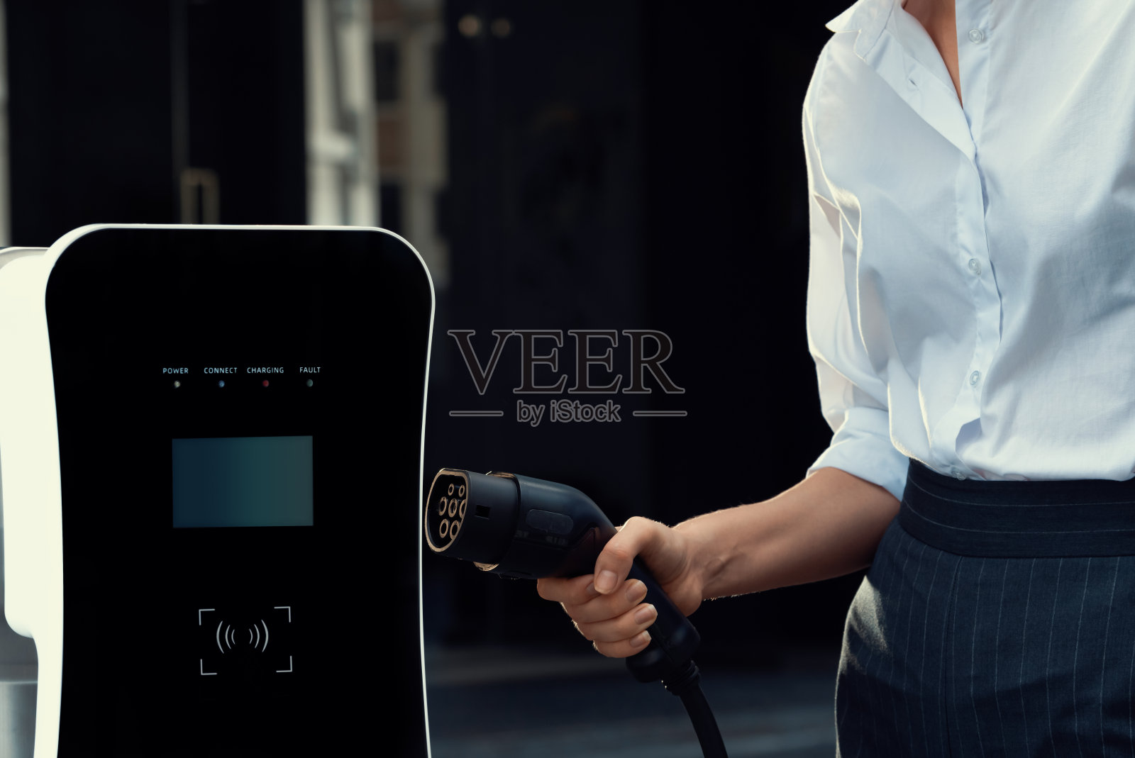 焦点电动车充电器插头与模糊的进步妇女充电电动车的背景。照片摄影图片