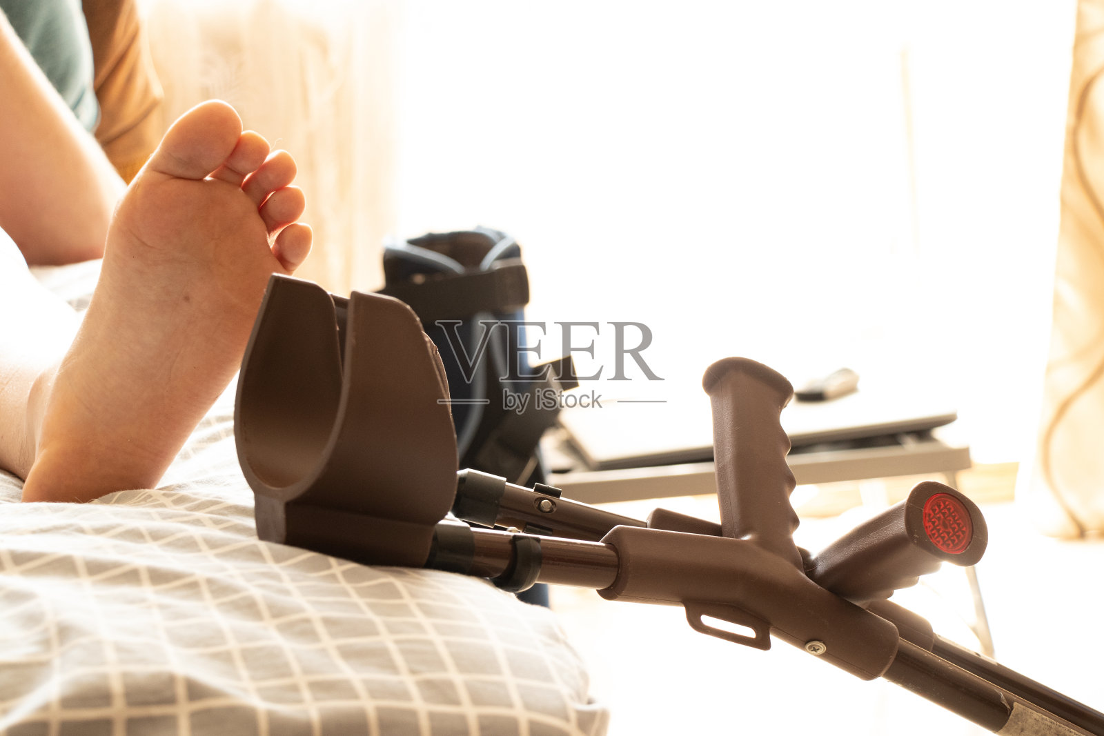 一名男子在手术后用膝盖和拐杖躺在公寓床旁的床上，双腿上缠着弹性绷带照片摄影图片