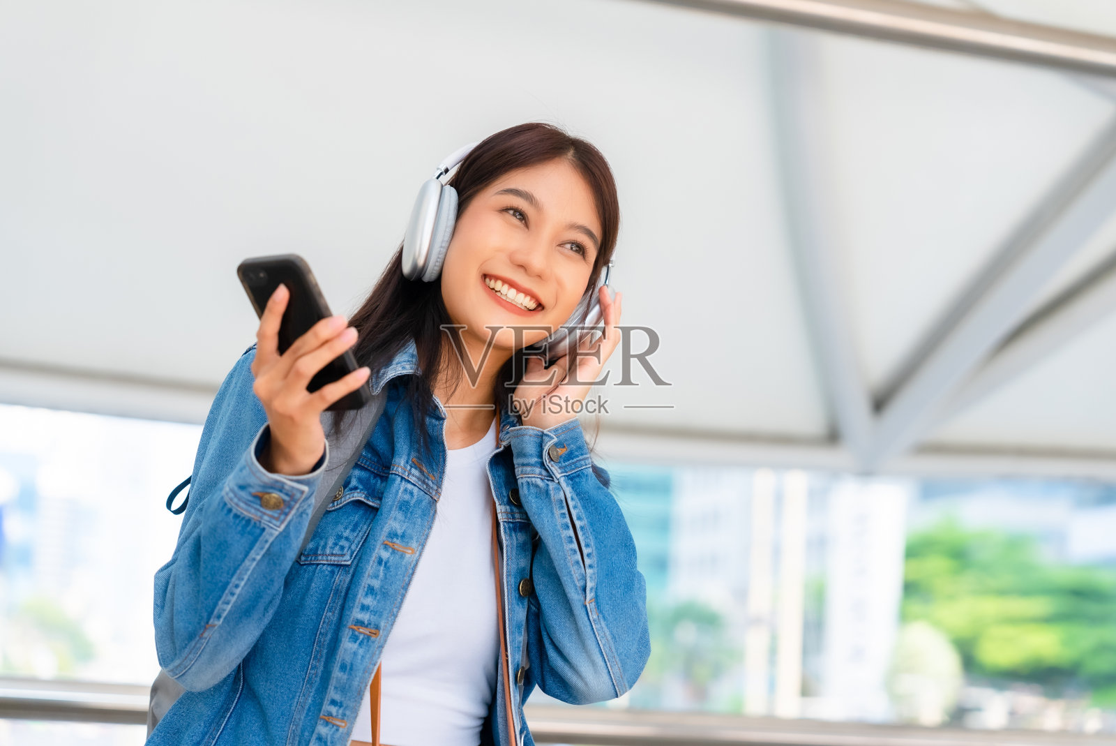 图为快乐的年轻亚洲女子在城市里用智能手机无线耳机上网听音乐照片摄影图片