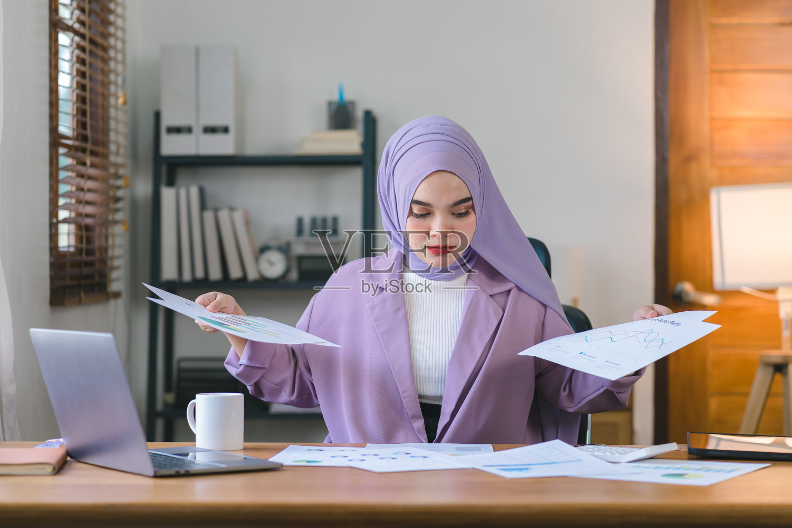 戴着紫色头巾在家用笔记本电脑工作的千禧一代穆斯林女商人看上去焦虑、疲惫、不知所措。照片摄影图片