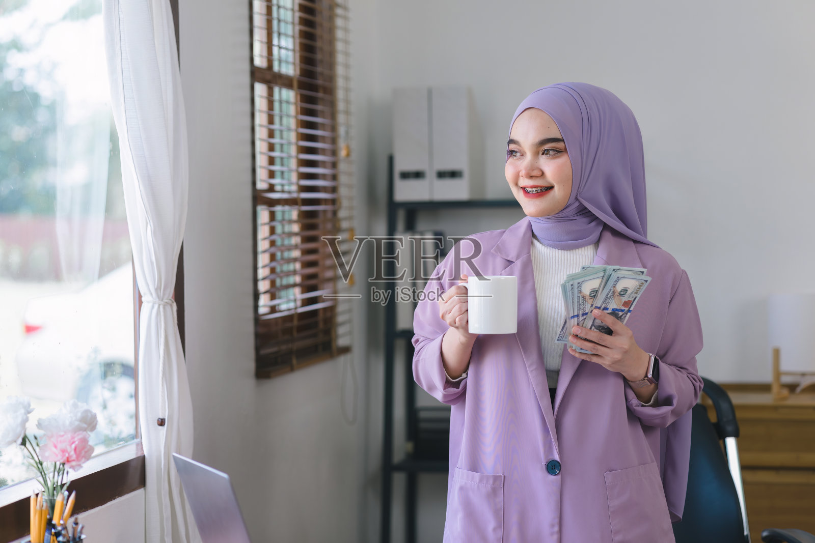 一个漂亮的穆斯林女商人戴着紫色的头巾，手里拿着很多钱。照片摄影图片