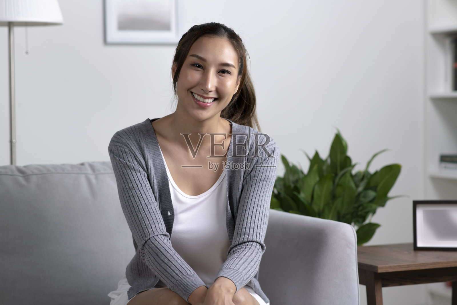 年轻快乐迷人的亚洲女人坐在家里的沙发上的肖像照片摄影图片