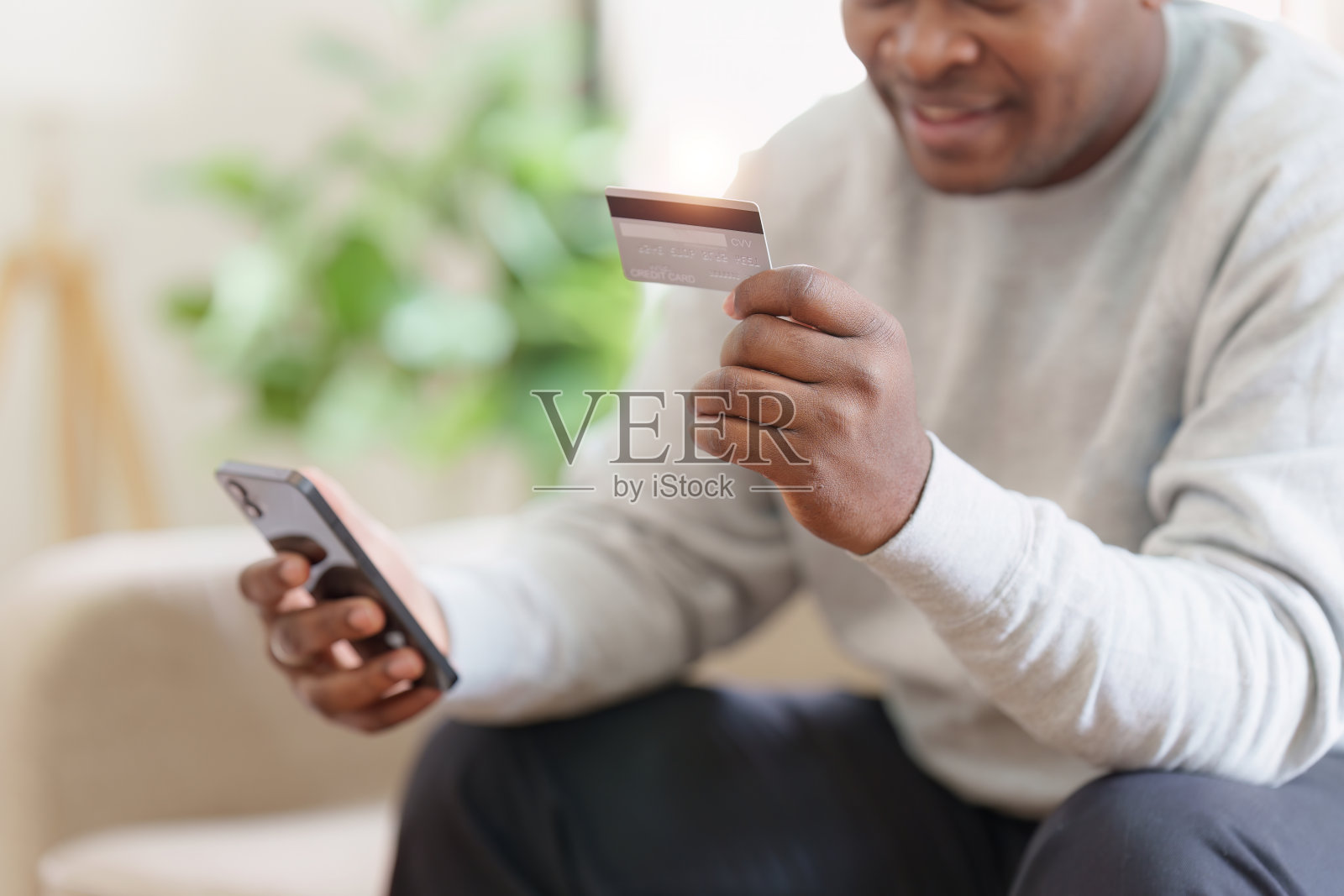 年轻的非洲裔美国人使用手机持有信用卡。银行应用，网上购物概念照片摄影图片