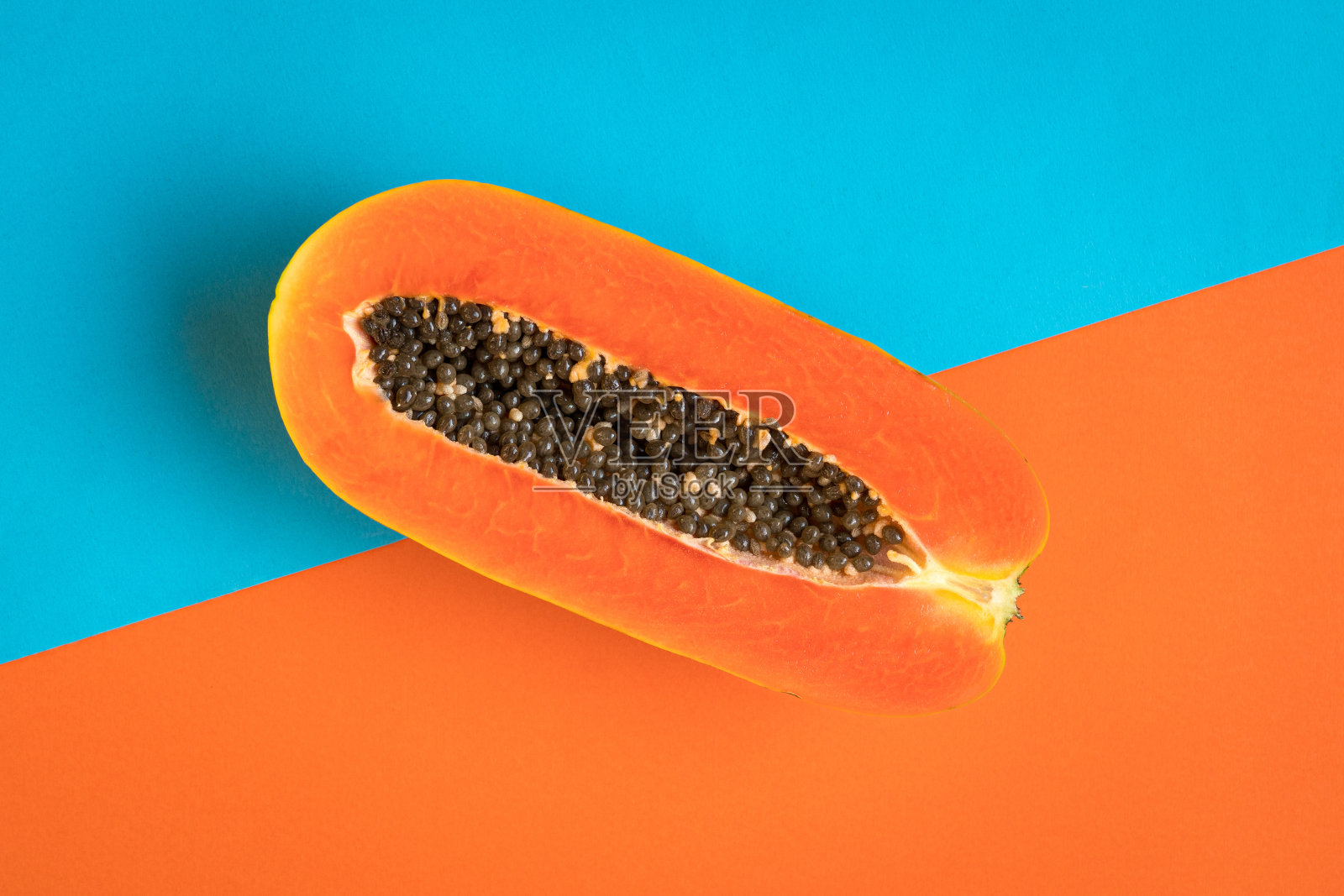 成熟的木瓜果实切成两半，蓝色和橙色的背景。照片摄影图片