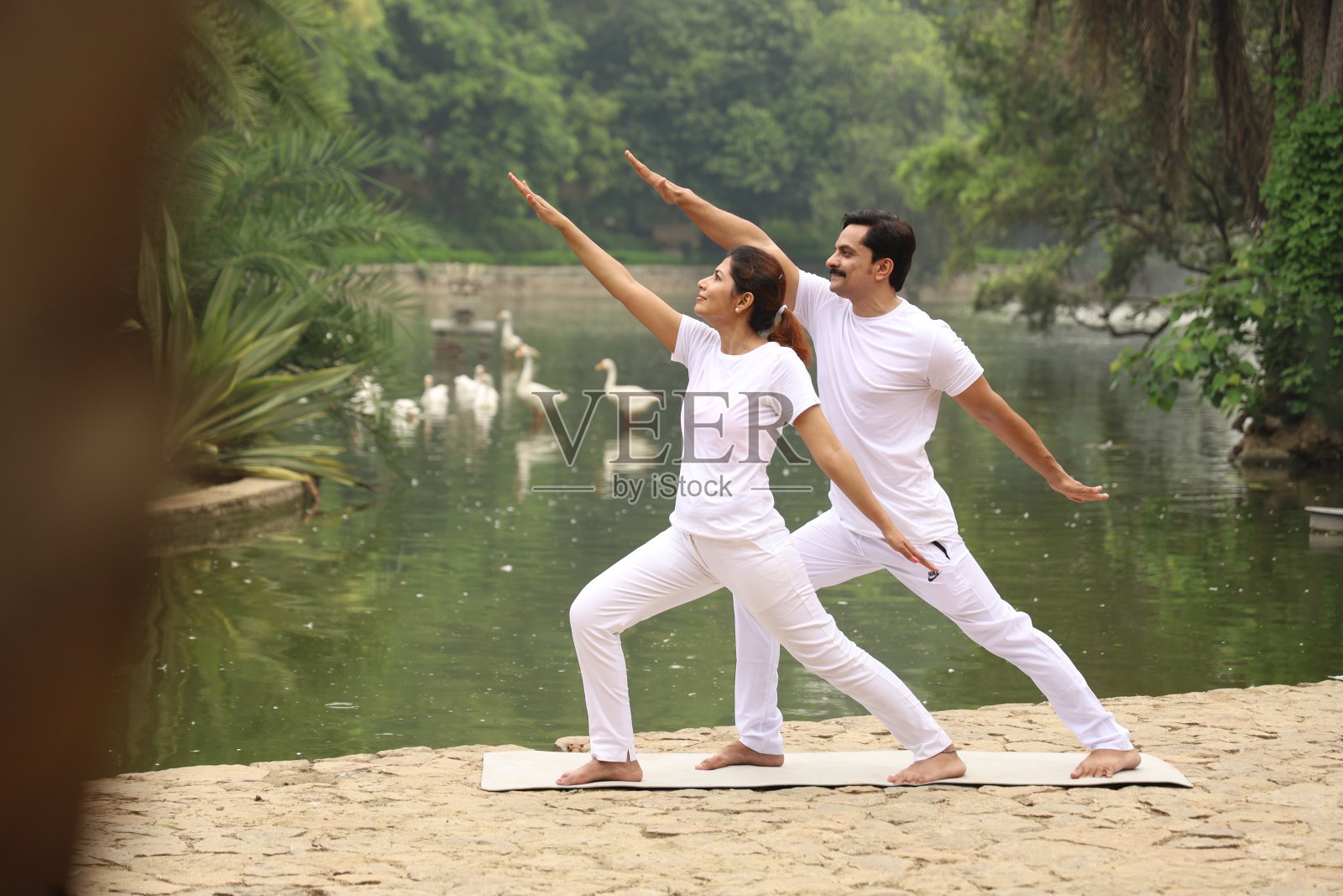 一对快乐的年轻夫妇在清晨的公园里，在绿色宁静的环境中冥想、锻炼和做瑜伽。照片摄影图片