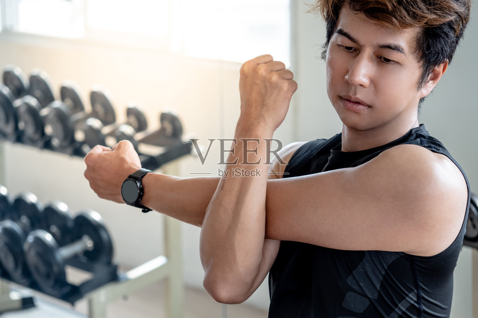 身穿黑色运动服的亚洲运动员，在健身房负重训练前伸展双臂，做斜肩伸展姿势。伸展肌肉的运动姿势。照片摄影图片