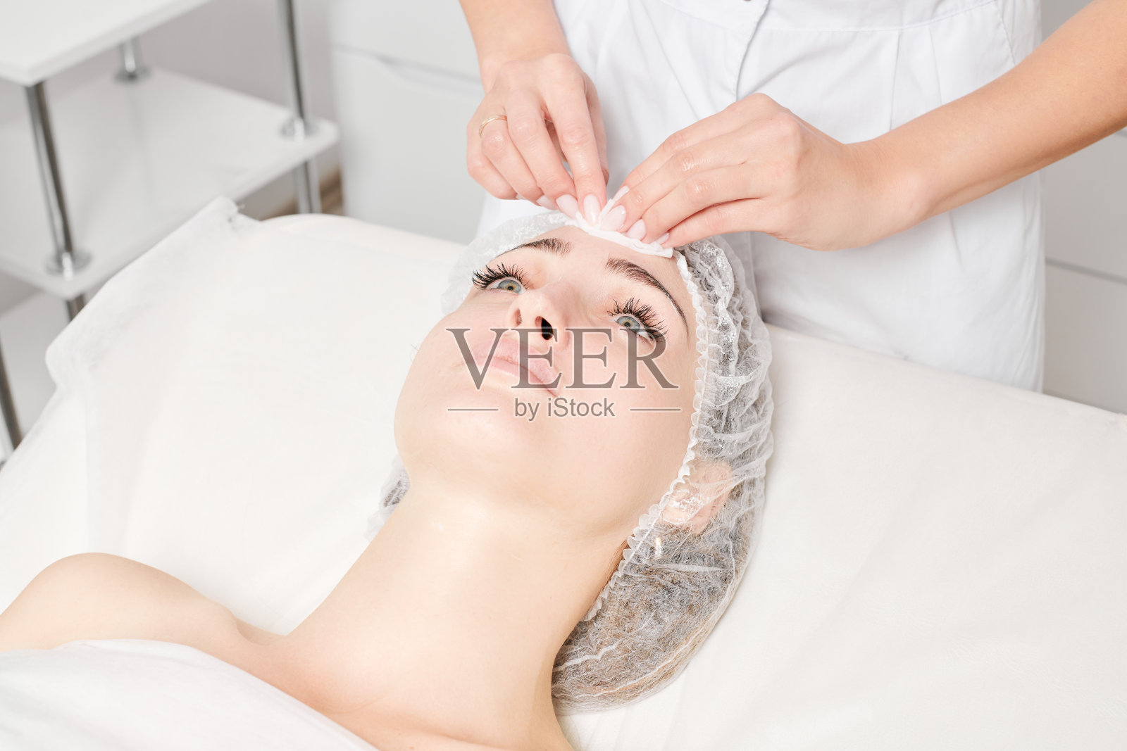 美容院美容师用化妆湿巾从女士脸上去除面霜面膜照片摄影图片