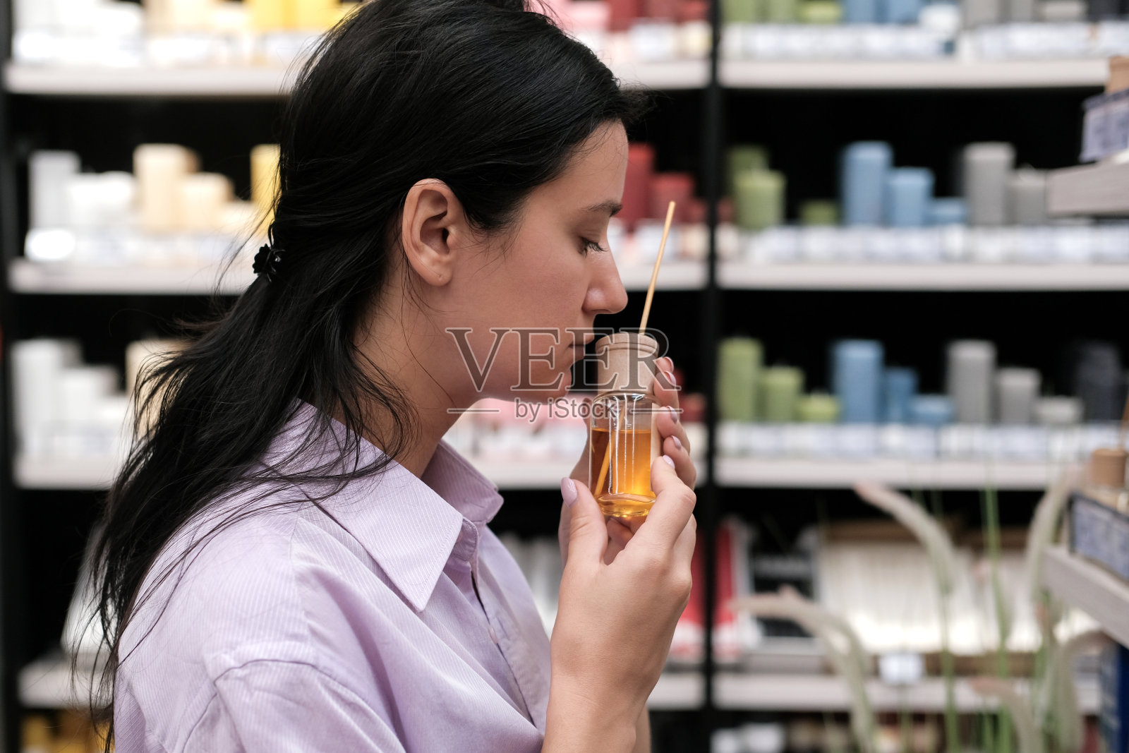 年轻的女顾客在店里闻着和选择芳香的芦苇扩散器。香氛扩散器玻璃瓶在商店出售。家居装饰和舒适的概念照片摄影图片