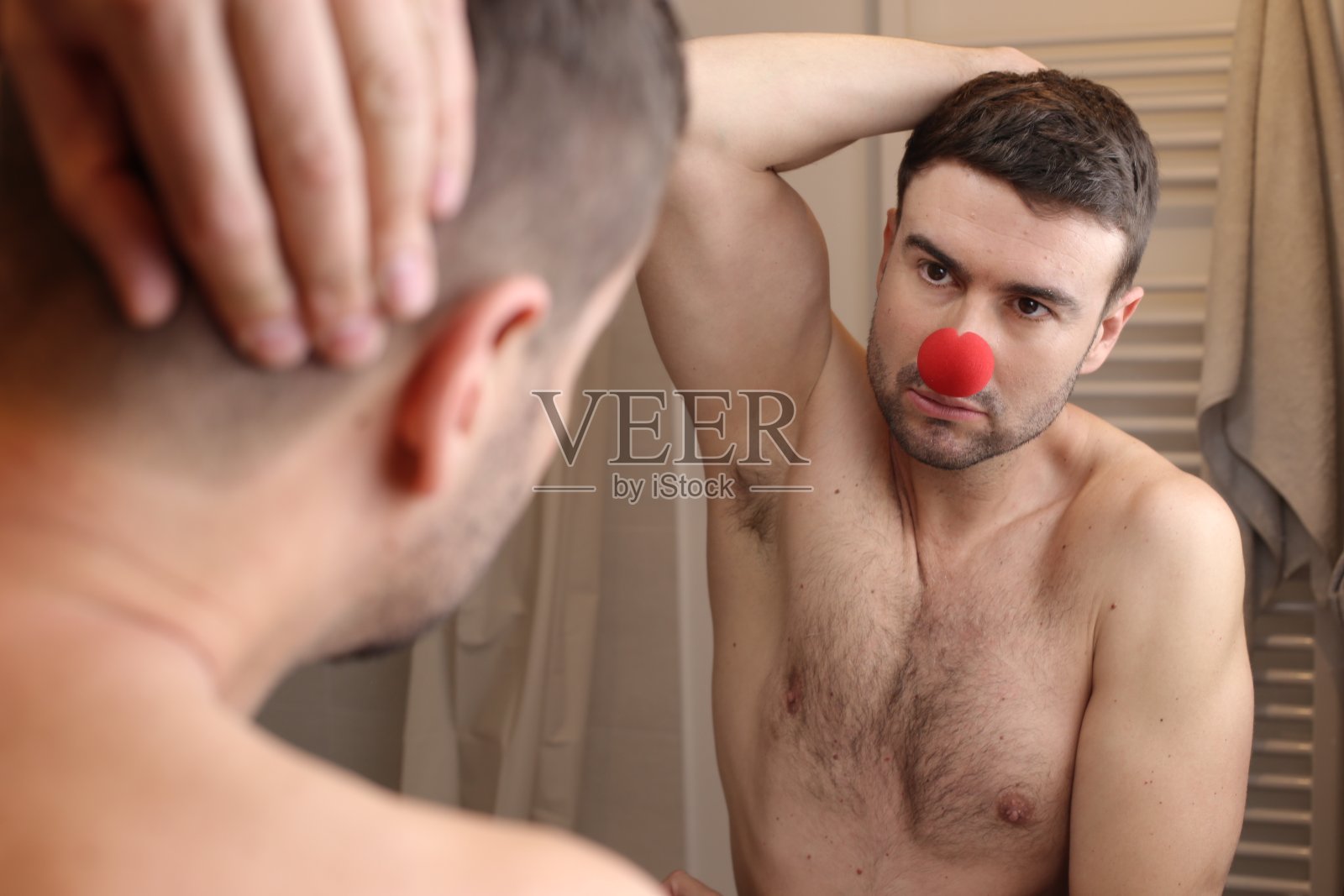 戴着小丑鼻子的男人看着自己的倒影照片摄影图片