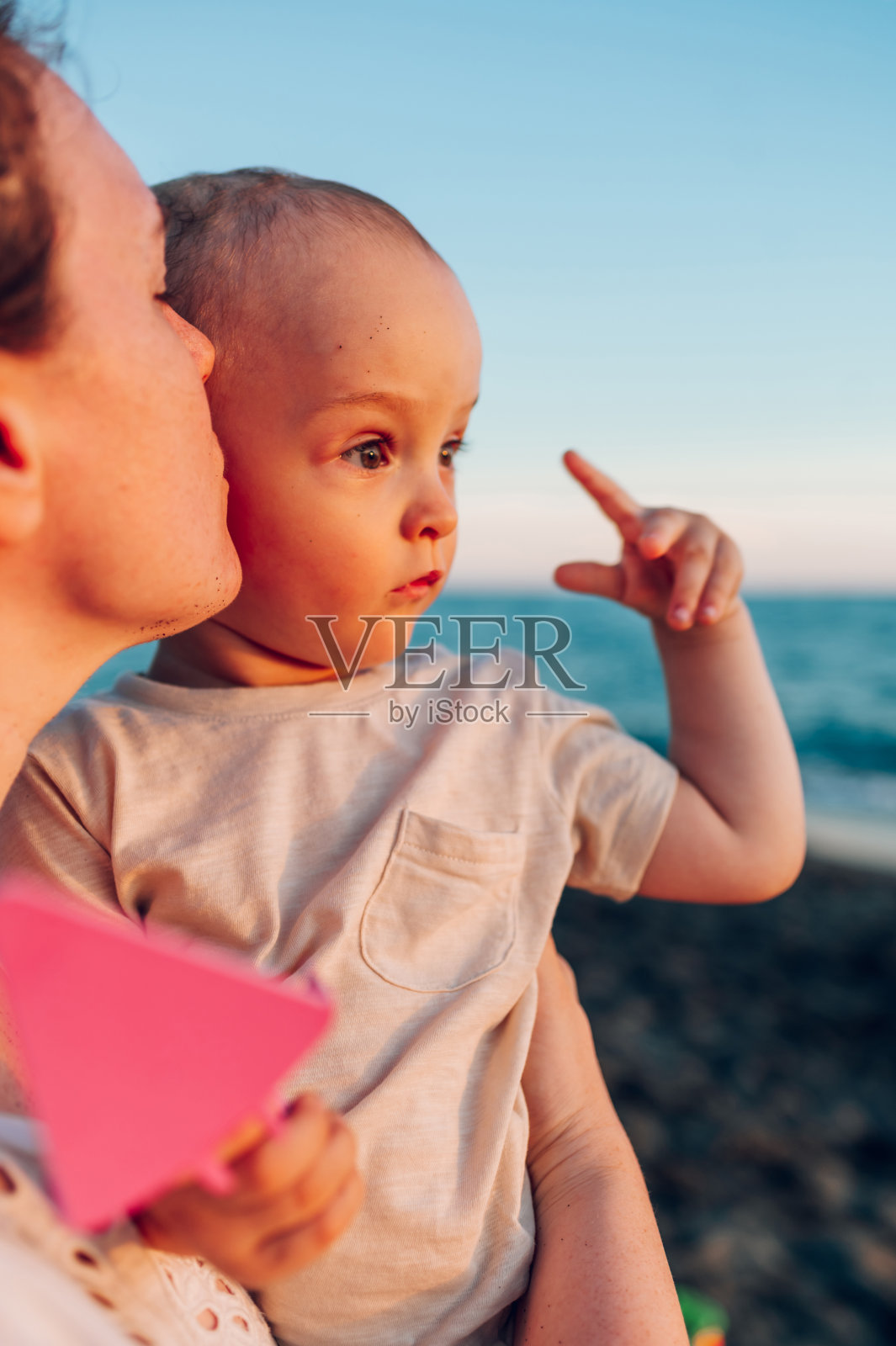 一位年轻的母亲在海滩上亲吻她沉思的儿子的特写镜头。照片摄影图片