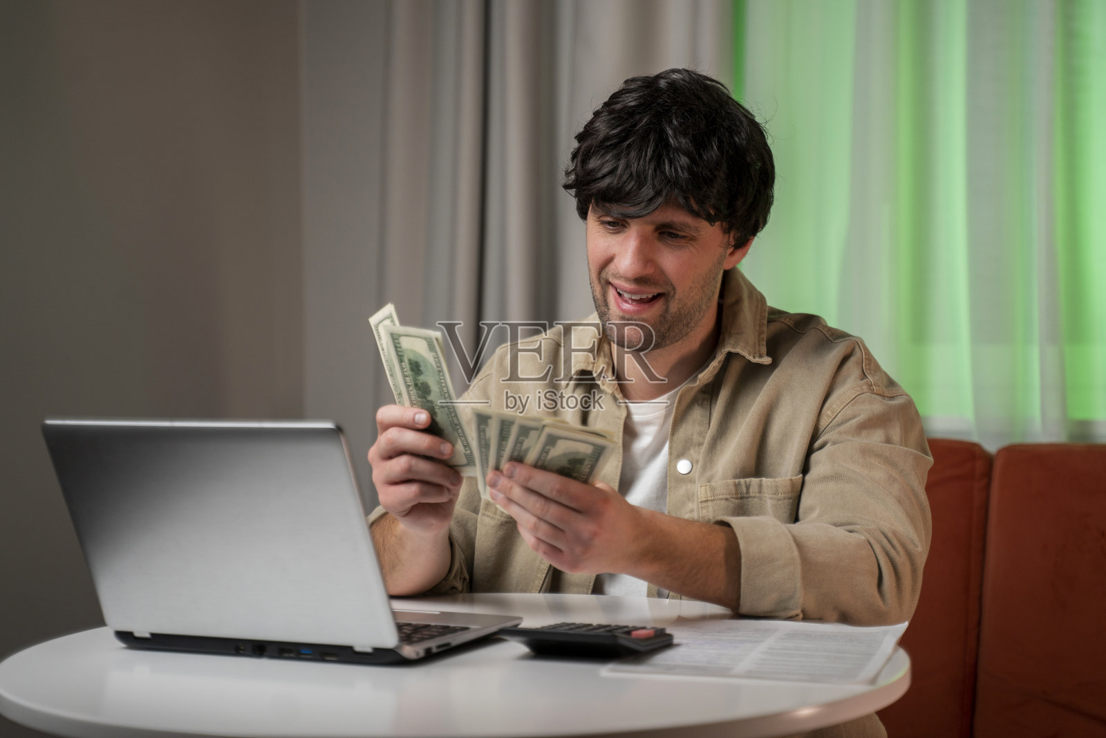 成功的商人坐在客厅里数钱。这个人赢了一大笔现金工资单。照片摄影图片