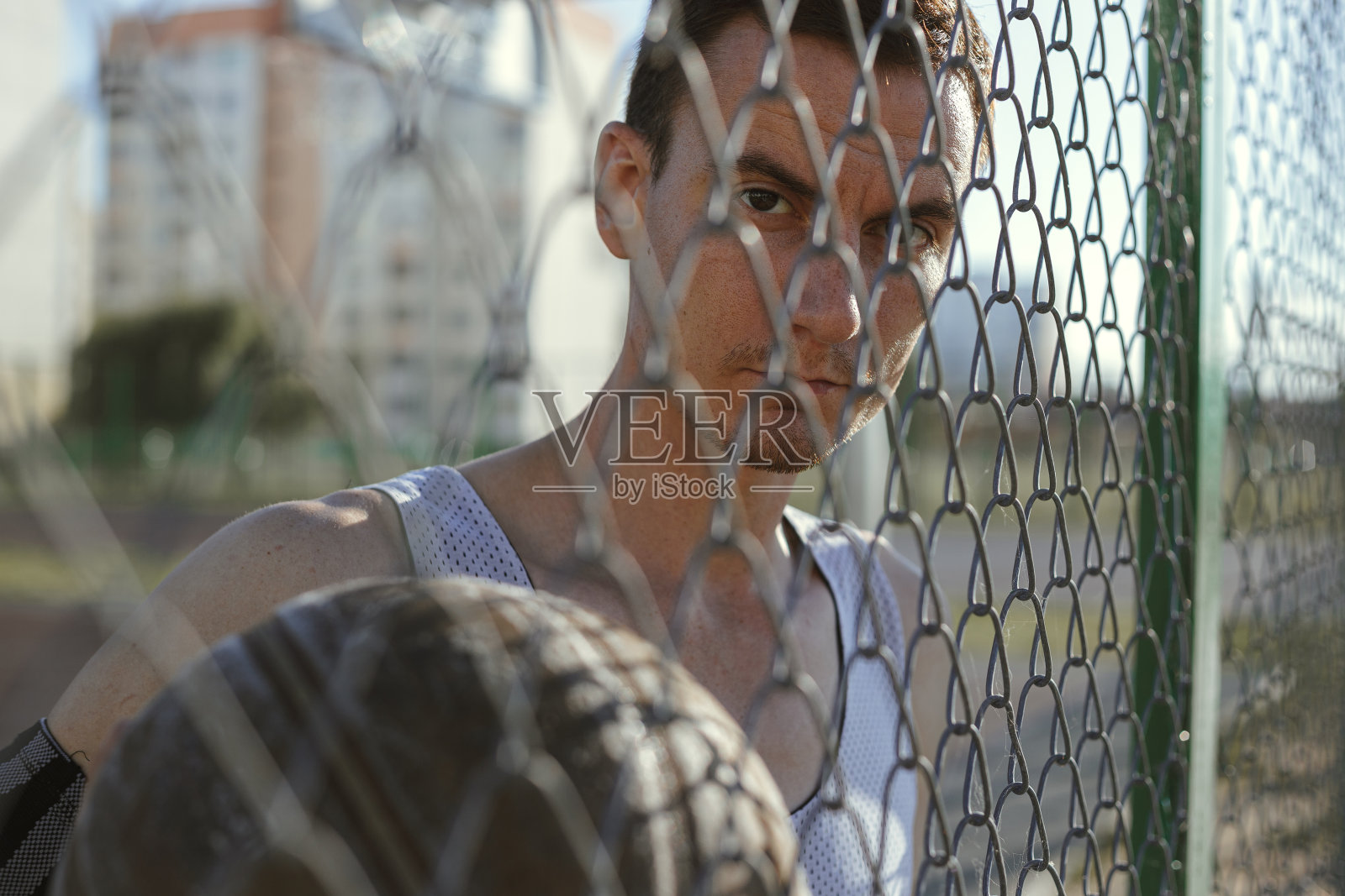 一名男子篮球运动员站在运动场的栅栏后面，拿着球照片摄影图片