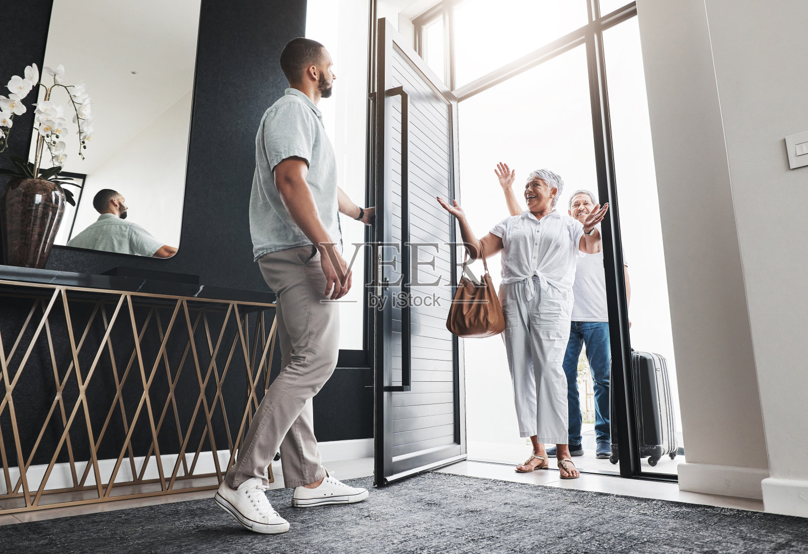 男人开门，家人来访，带着微笑度假，爱和团结在一起，关心和度假。恋爱时，男主邀请父母带着喜悦和幸福进家门，兴奋时带着问候和欢迎照片摄影图片