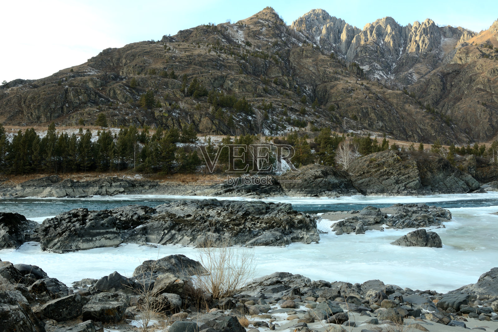 在一个阳光明媚的冬夜，一条美丽的山河流经雪山的山谷，中间的岩石形成。照片摄影图片