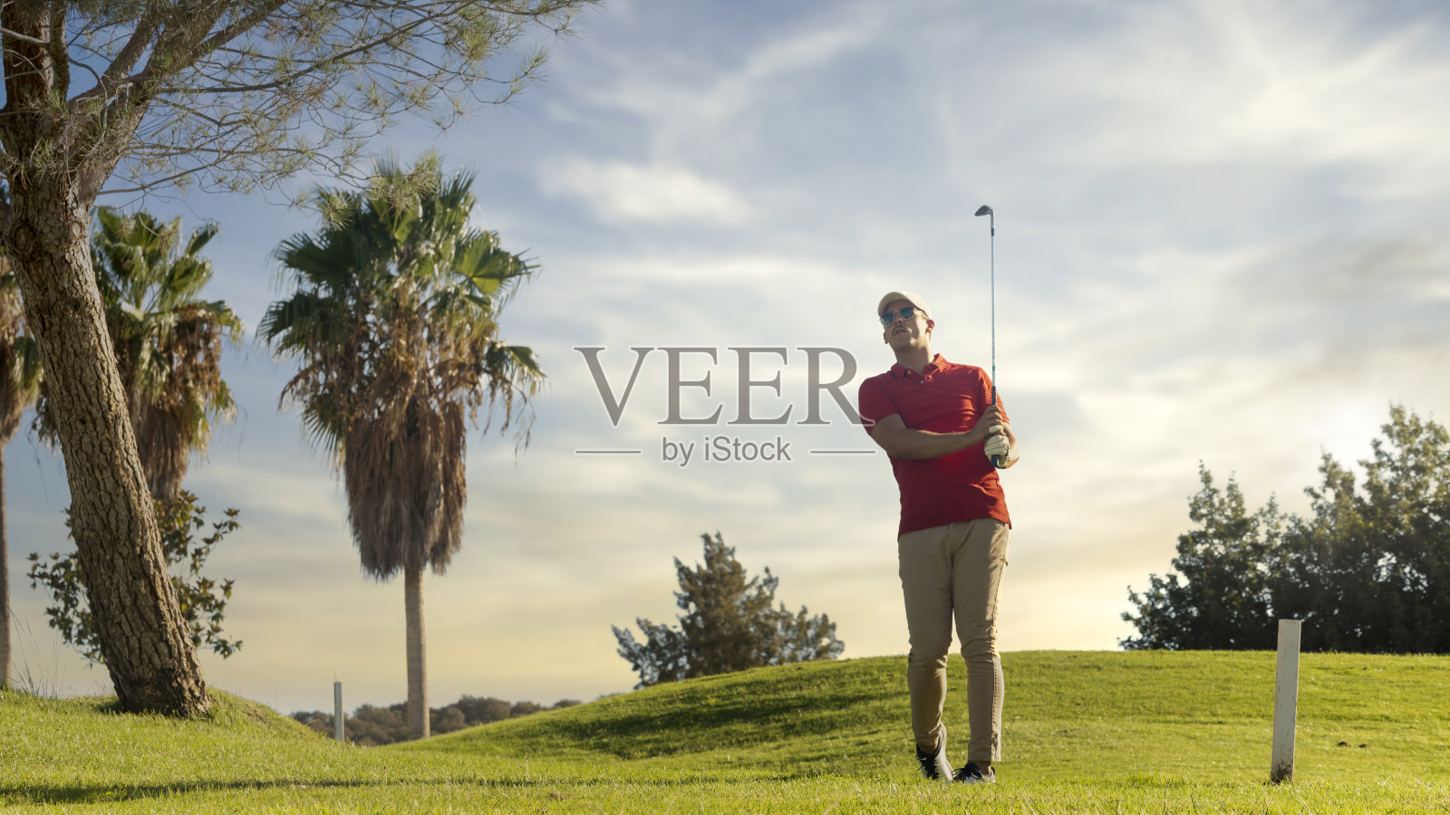 高尔夫球手练习运动。在一个阳光明媚的日子里，一名高尔夫球手在以绿草和棕榈树为背景的高尔夫球场上击球。运动与健康理念。本空间照片摄影图片