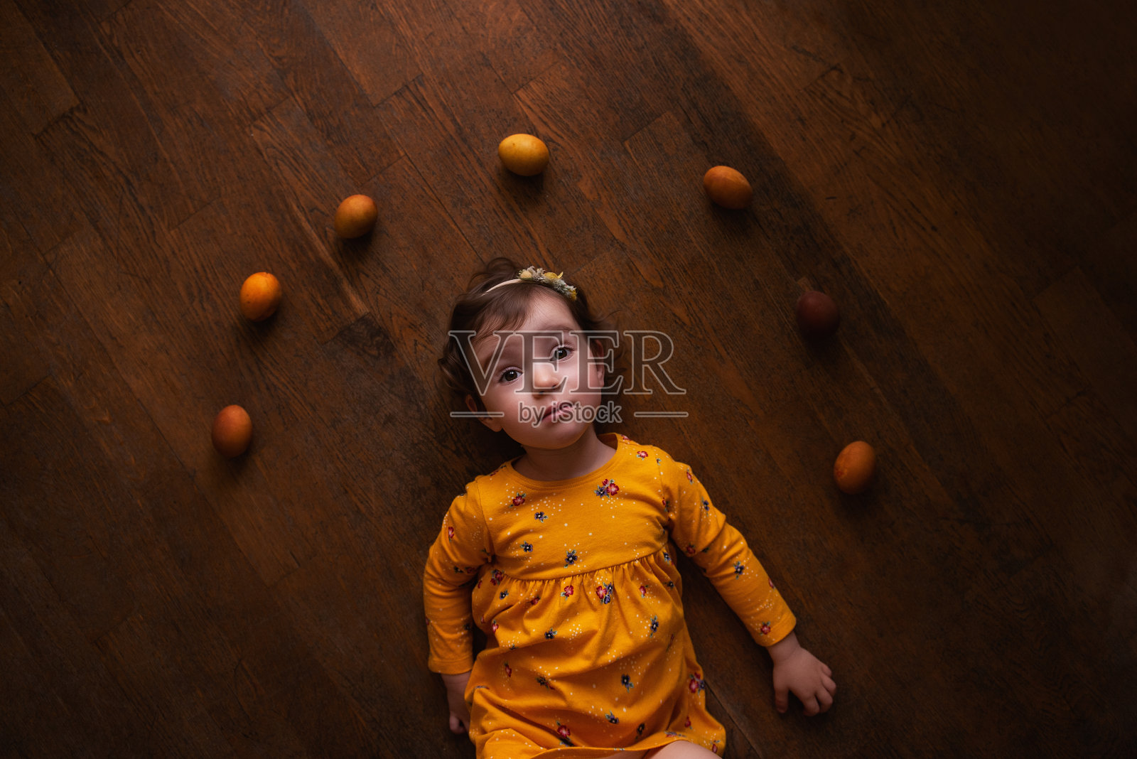 小女孩穿着衣服躺在棕色的木地板上，旁边是涂着姜黄颜料的复活节彩蛋照片摄影图片