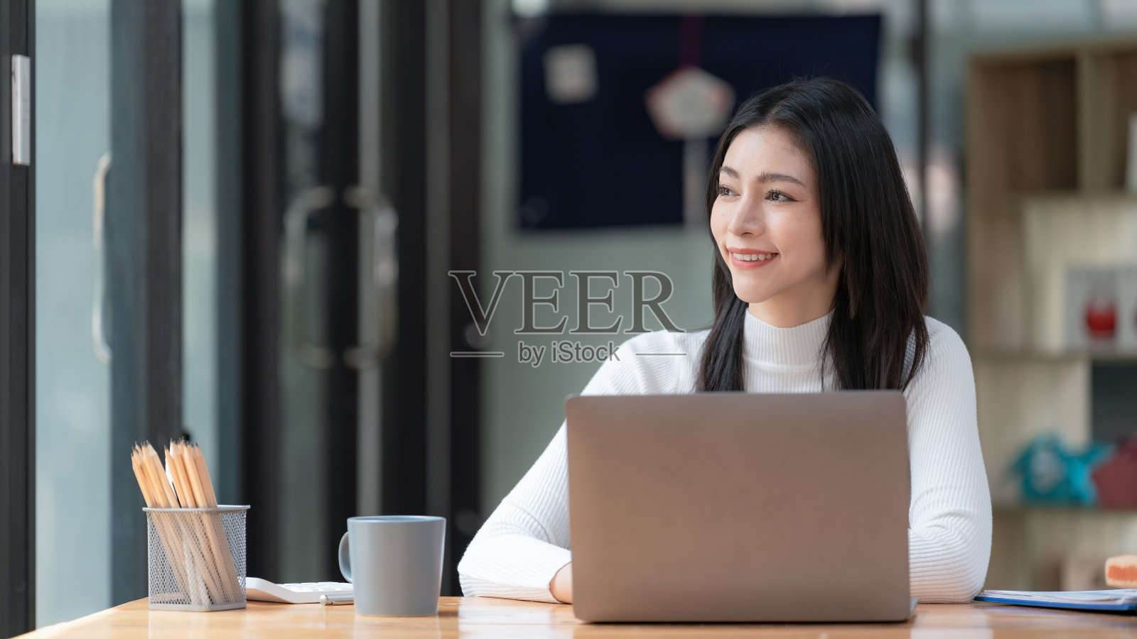 一个亚洲女商人在现代办公室里用笔记本电脑工作时思考和看向别处的形象。照片摄影图片