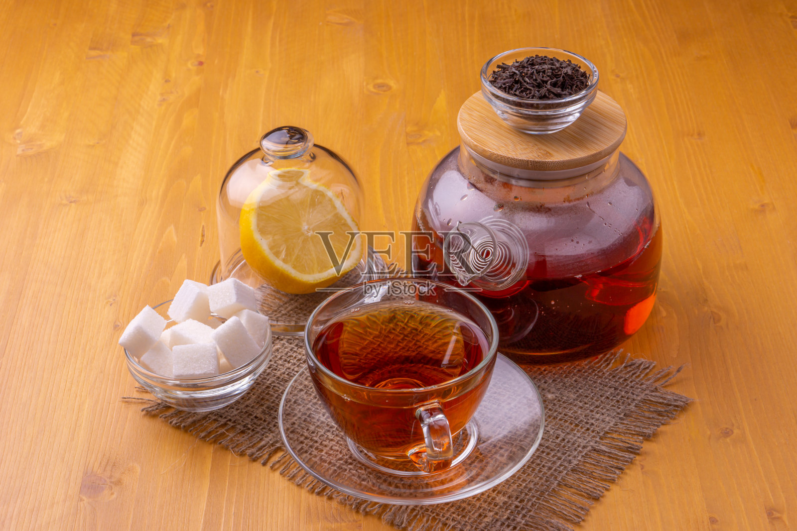 一个茶壶和一个盛红茶的玻璃杯。旁边是柠檬片和方糖。漂亮明亮的木制背景。照片摄影图片