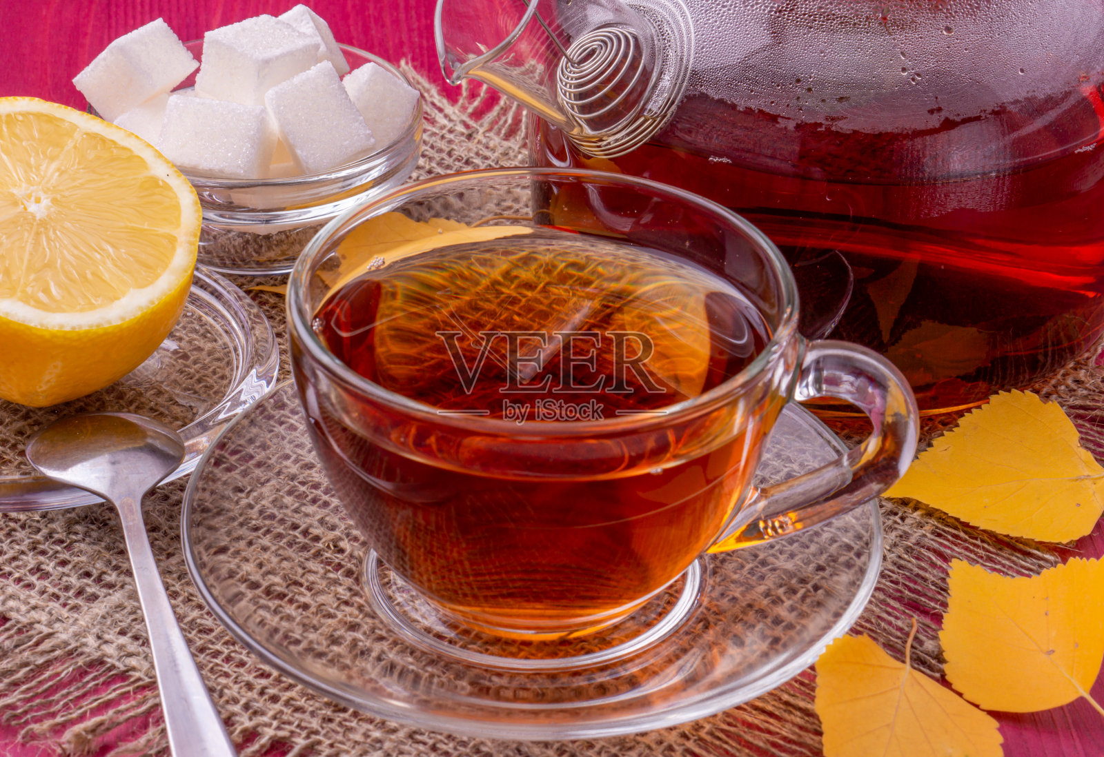 一个茶壶和一个盛红茶的玻璃杯。旁边是柠檬片和方糖。漂亮明亮的木制背景。照片摄影图片