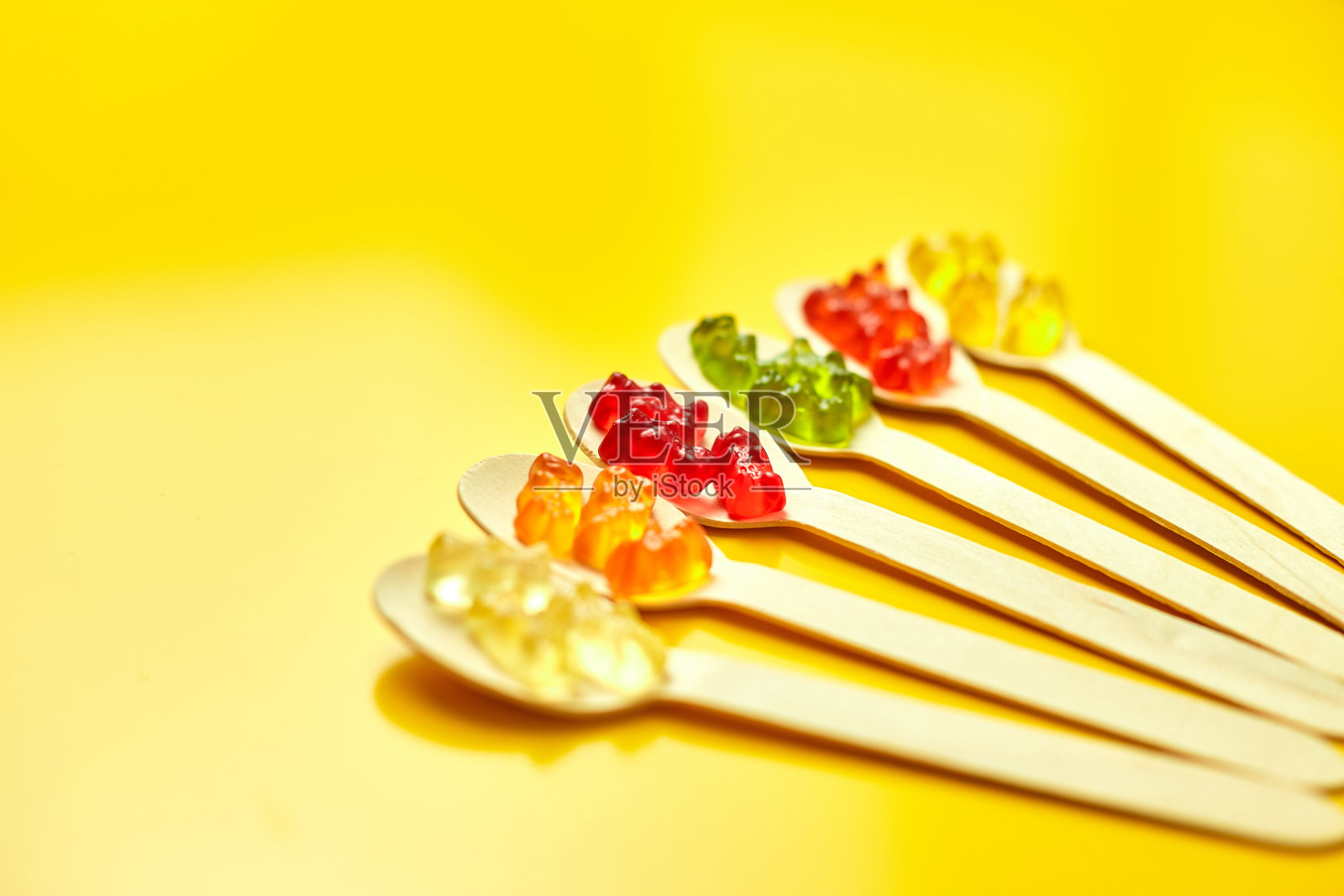 平铺构图与美味的果冻熊糖果在木勺，软糖熊在黄色背景，俯视图，复制空间。照片摄影图片