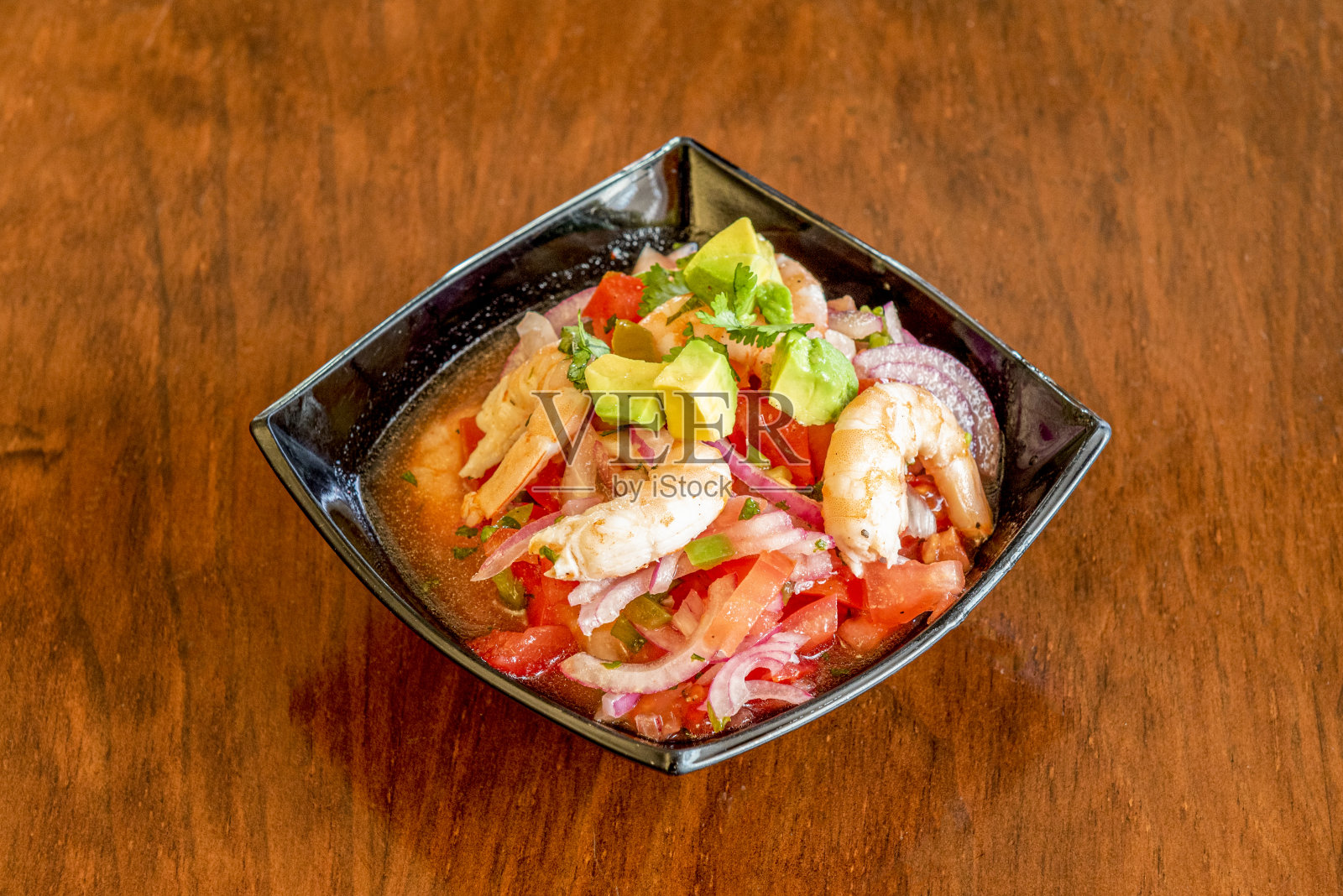 黑碗里的酸橘汁腌鱼配上大虾，番茄，鳄梨，欧芹照片摄影图片