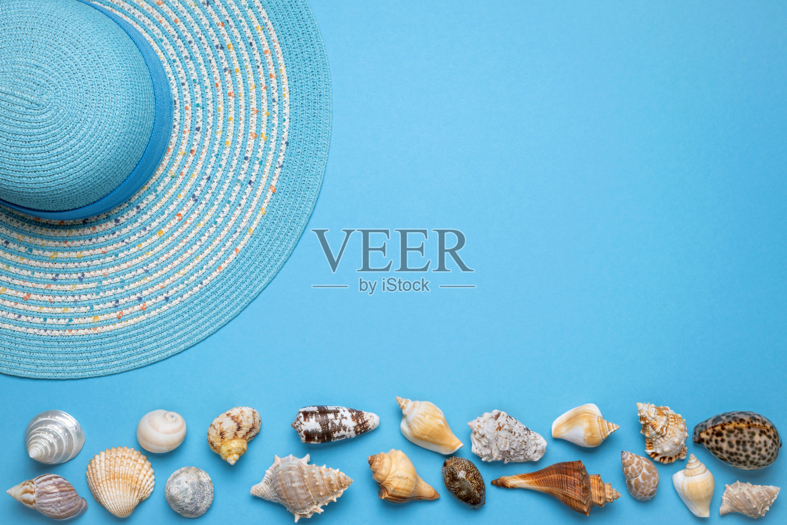 夏天和假期平躺着一个美丽的蓝色条纹女人草帽和各种贝壳在蓝色背景的图片下缘。照片摄影图片