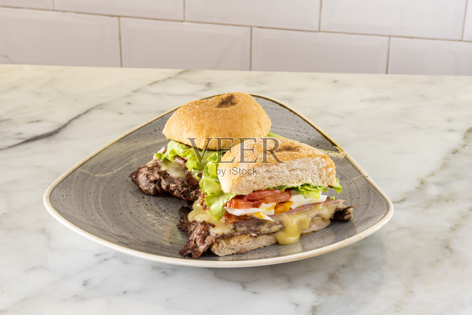 烤羊肉和烟熏培根三明治，配上融化的奶酪、切碎的煮鸡蛋、卷心莴苣和番茄片，放在一个大大理石桌子上照片摄影图片