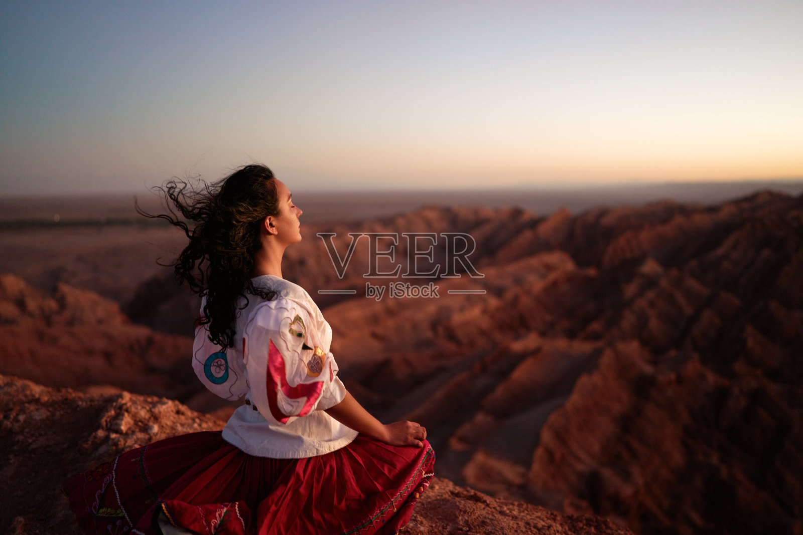 在圣佩德罗德阿塔卡马，中年成年拉丁裔妇女穿着前西班牙土著文化或玻利维亚乔拉的服装，坐在月亮谷的瞭望处照片摄影图片