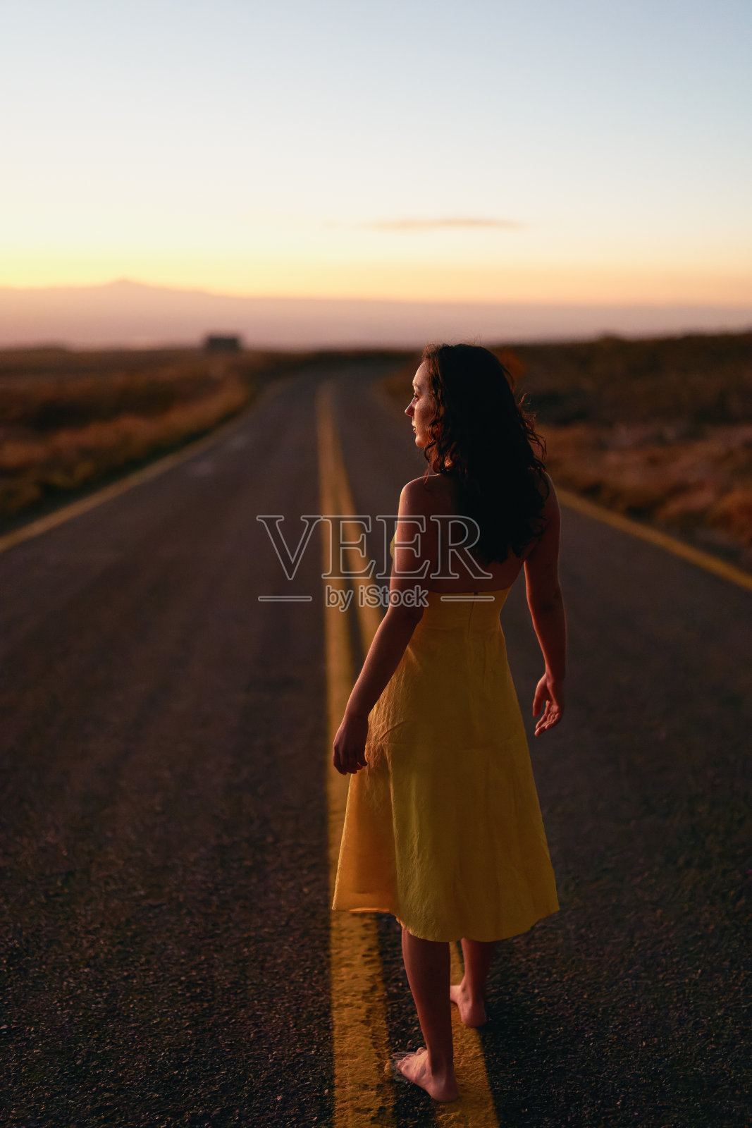 在los flamencos国家保护区的高原上，年轻女子赤脚走在路上，穿着黄色的衣服照片摄影图片
