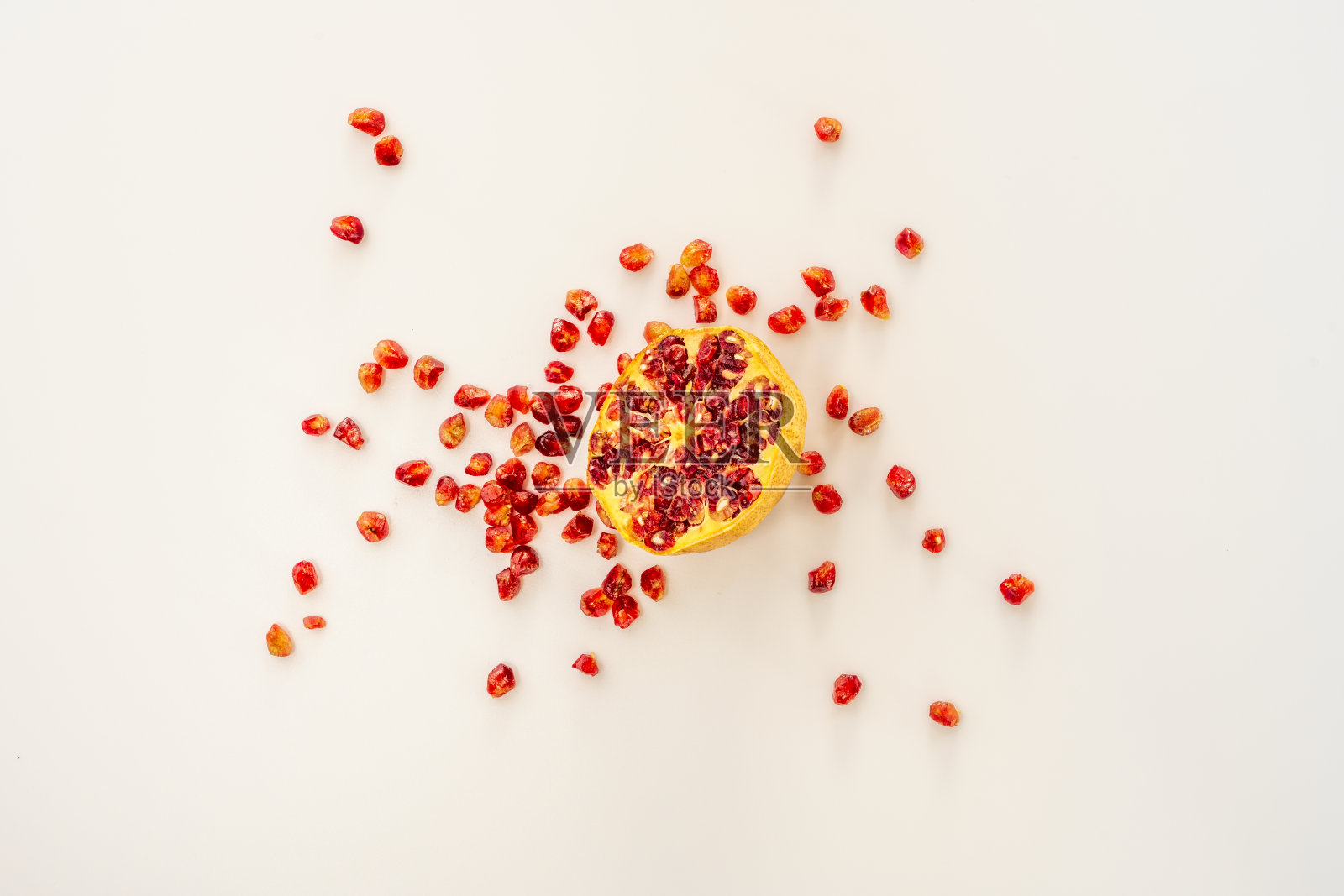半截石榴的俯视图，白色的背景上散落着美味的红豆。照片摄影图片