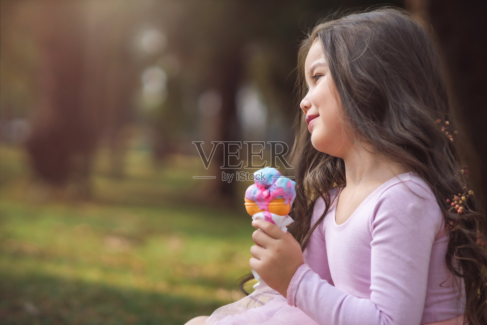 可爱的金发卷发女孩在公园里吃着美味的冰淇淋，儿童节的概念，复制空间照片摄影图片