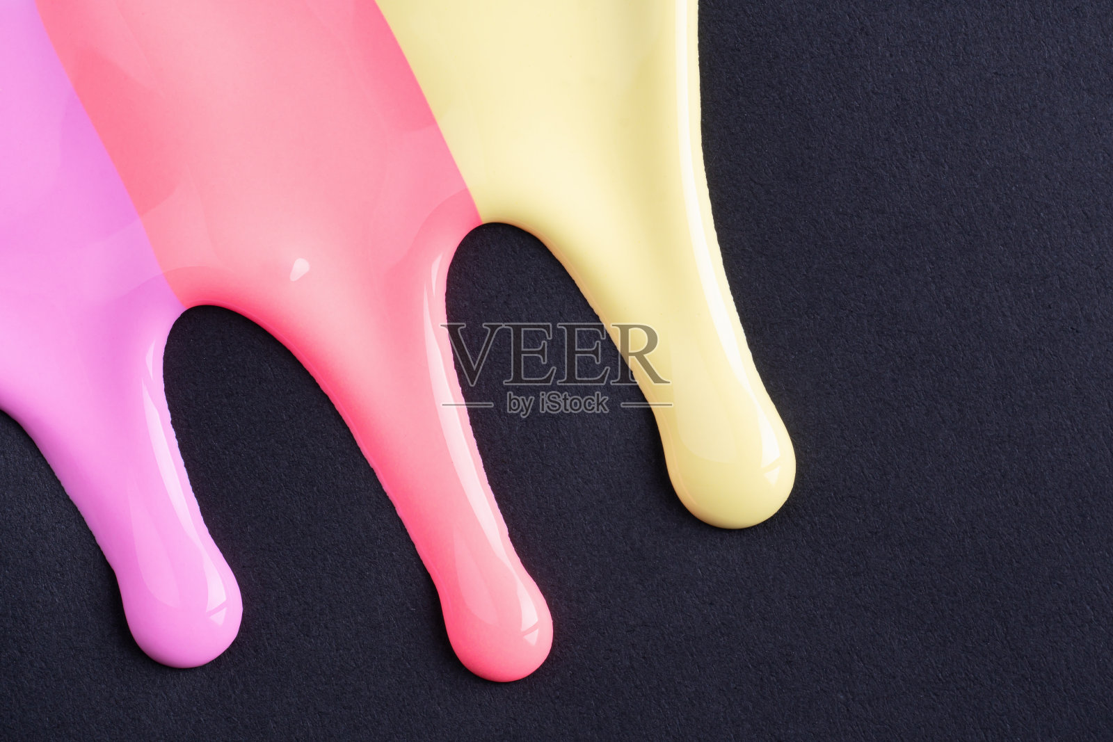 彩虹色的液体滴在黑色的纸上流淌。抽象艺术。五颜六色的油漆滴在黑色的墙上照片摄影图片