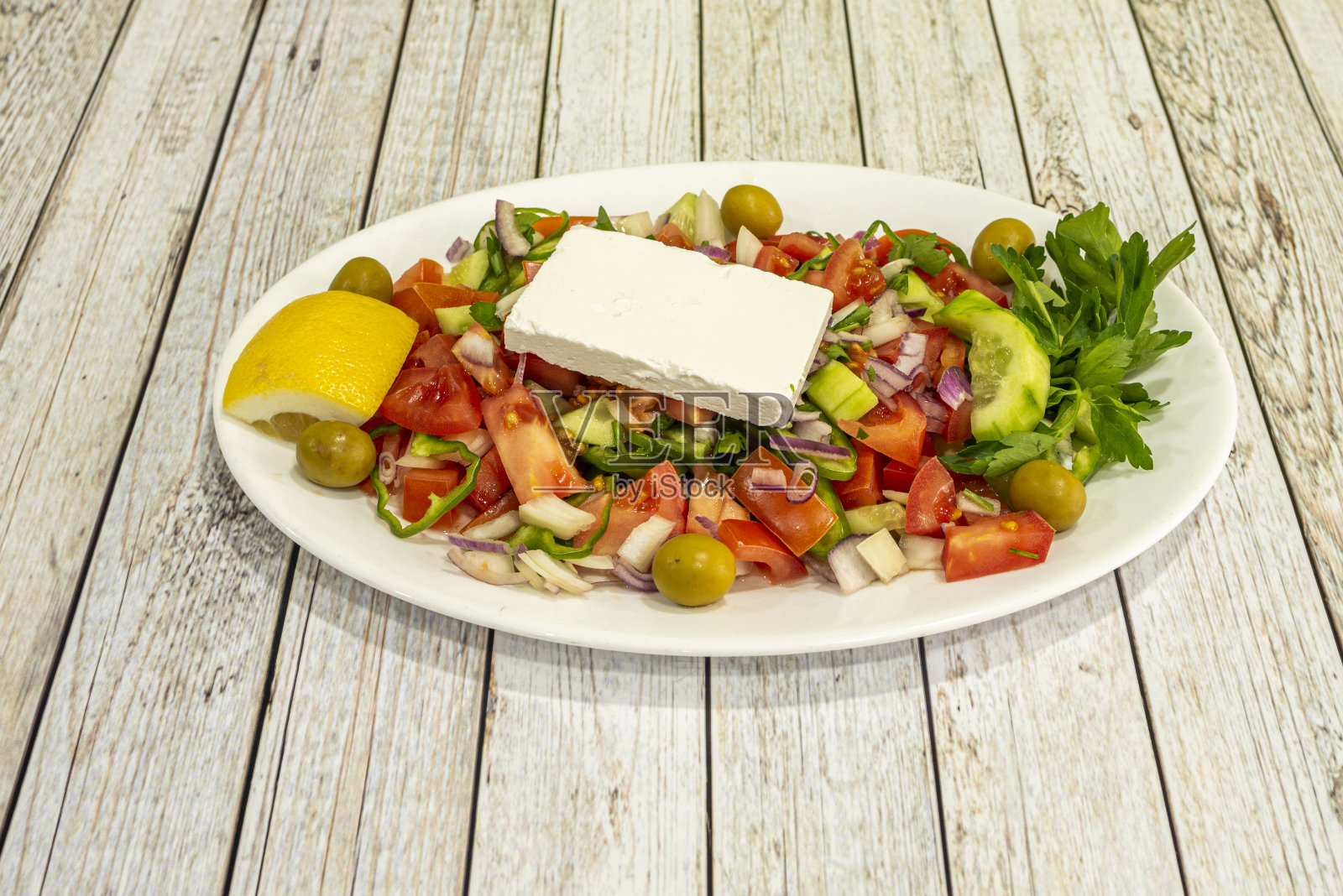 地中海沙拉托盘，配有新鲜奶酪，黄瓜和番茄碎，绿橄榄，黄瓜和红洋葱，柠檬和新鲜欧芹。照片摄影图片