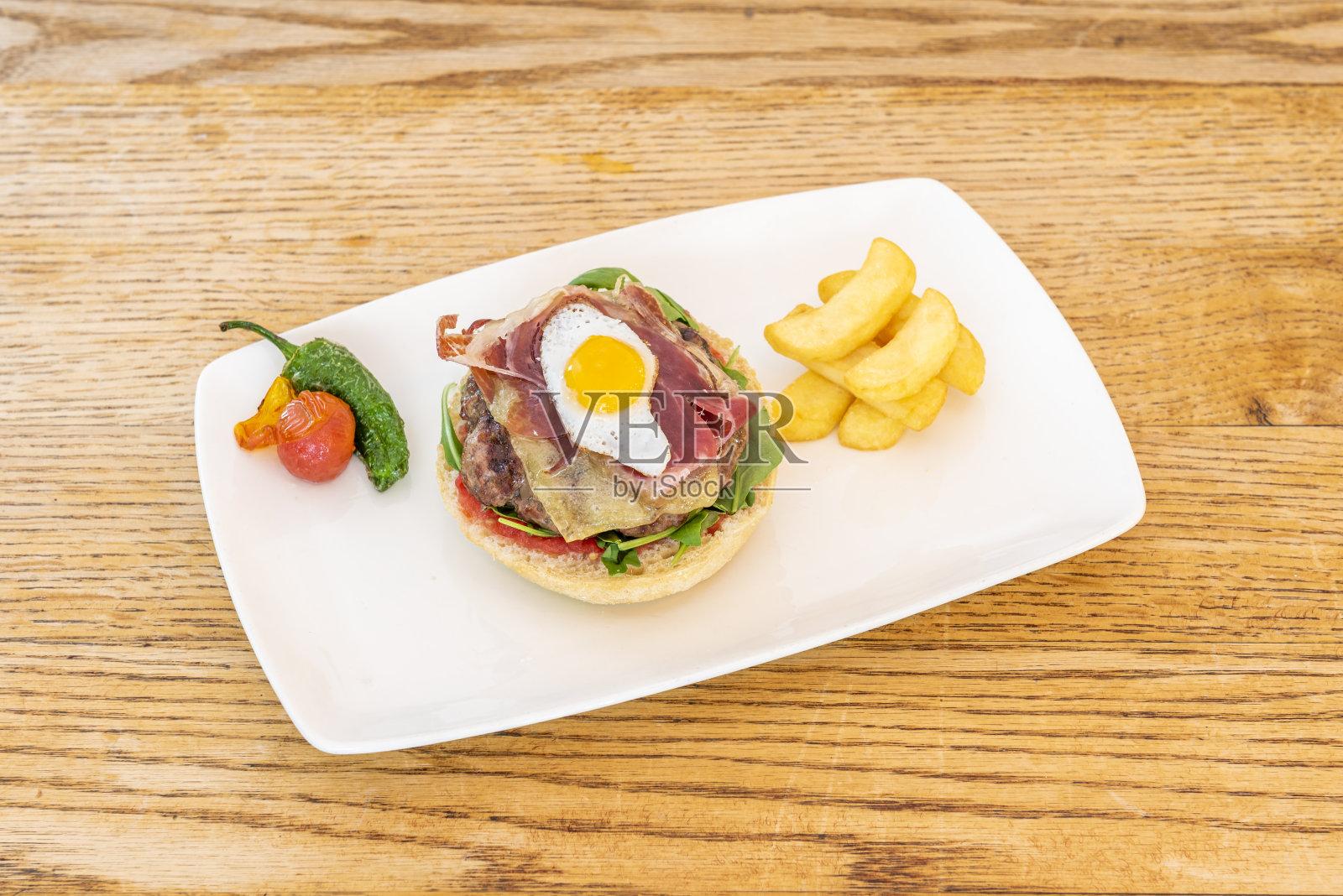 牛肉汉堡配上融化的奶酪，塞拉诺火腿片，芝麻菜，鹌鹑蛋，炸辣椒配土豆照片摄影图片