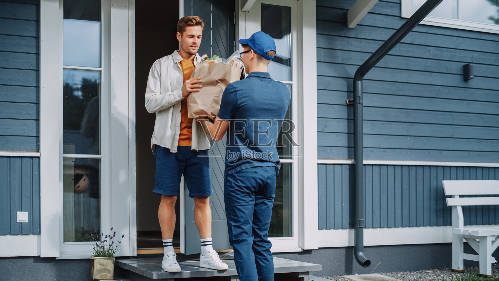 一个在杂货店送货服务的年轻人的肖像，带着一袋新鲜蔬菜和其他食品到一个居民区的家。收件人在平板电脑上签署了一份弃权书。照片摄影图片