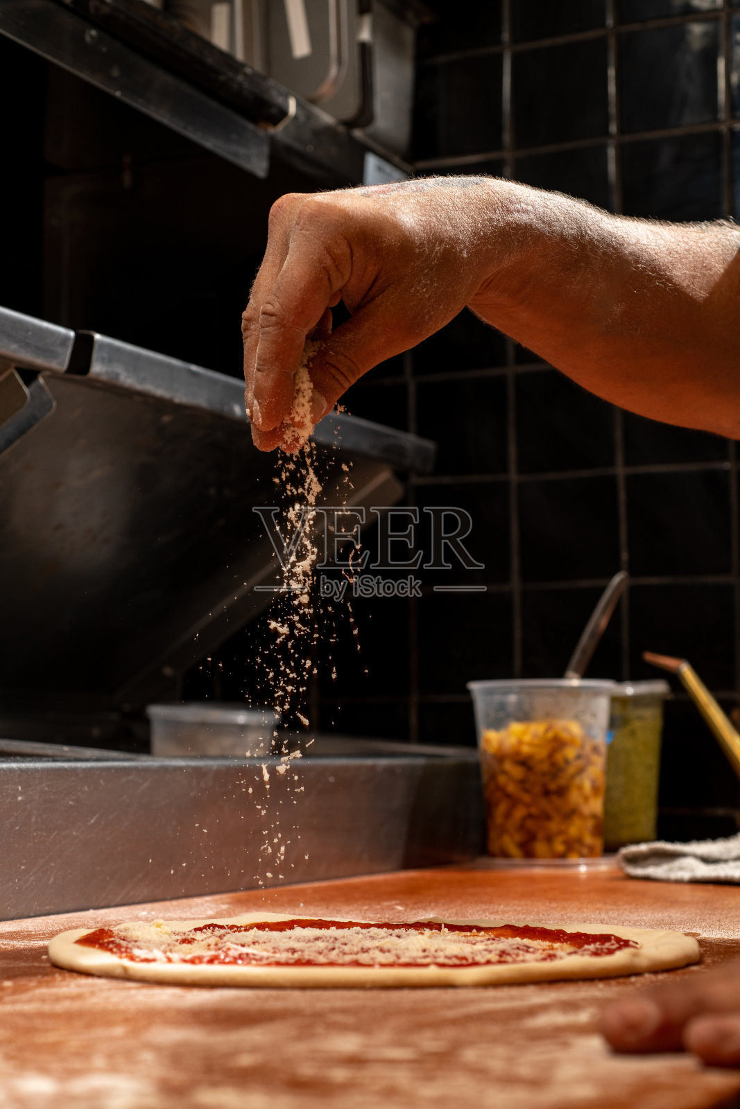 在未烤的披萨上洒上帕玛森奶酪。照片摄影图片