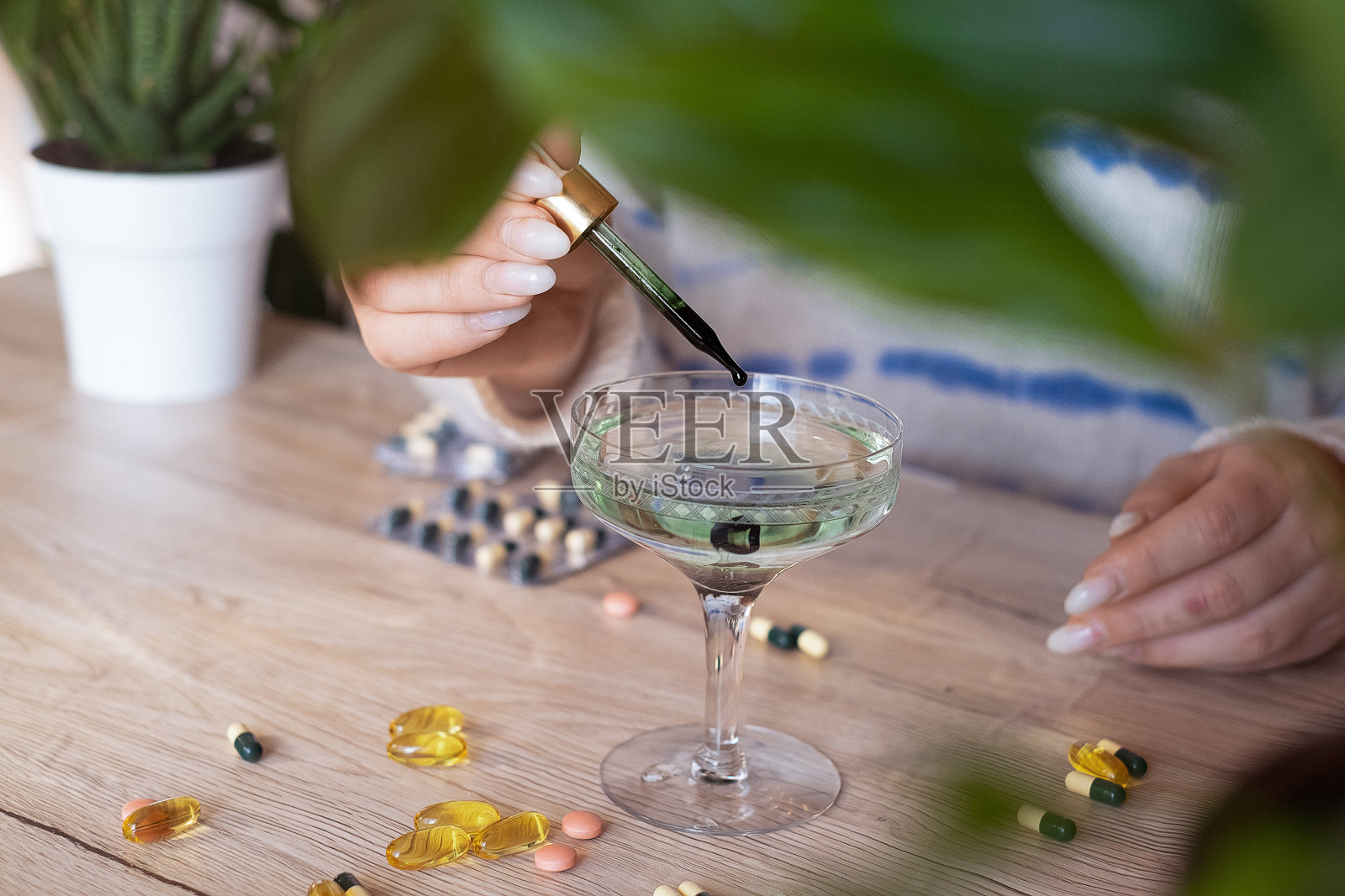 一位身穿白色毛衣的妇女站在棕榈树旁，往一杯水中加入叶绿素照片摄影图片