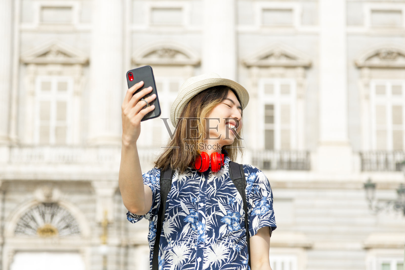 微笑的年轻亚洲游客戴着帽子和耳机自拍。照片摄影图片