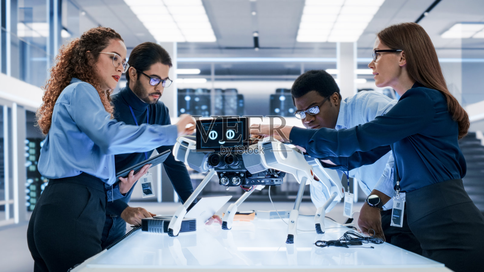 专业的国际男女工程师团队在工厂开发车间使用工业可编程机器狗。技术设施，机器，计算机和研究设备。照片摄影图片