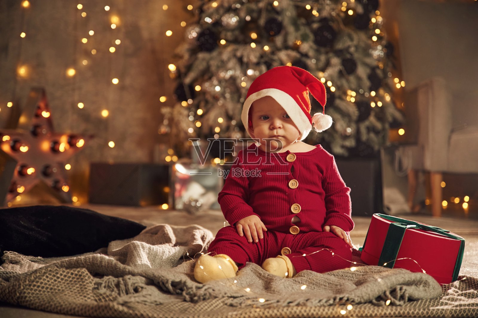 穿着节日服装，戴着圣诞帽。可爱的小婴儿在家。新年装饰。假期的概念照片摄影图片
