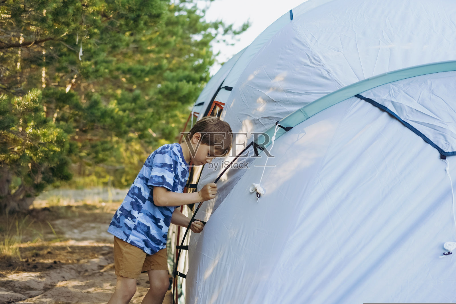 可爱的白人小男孩在帮忙搭帐篷。家庭露营概念照片摄影图片