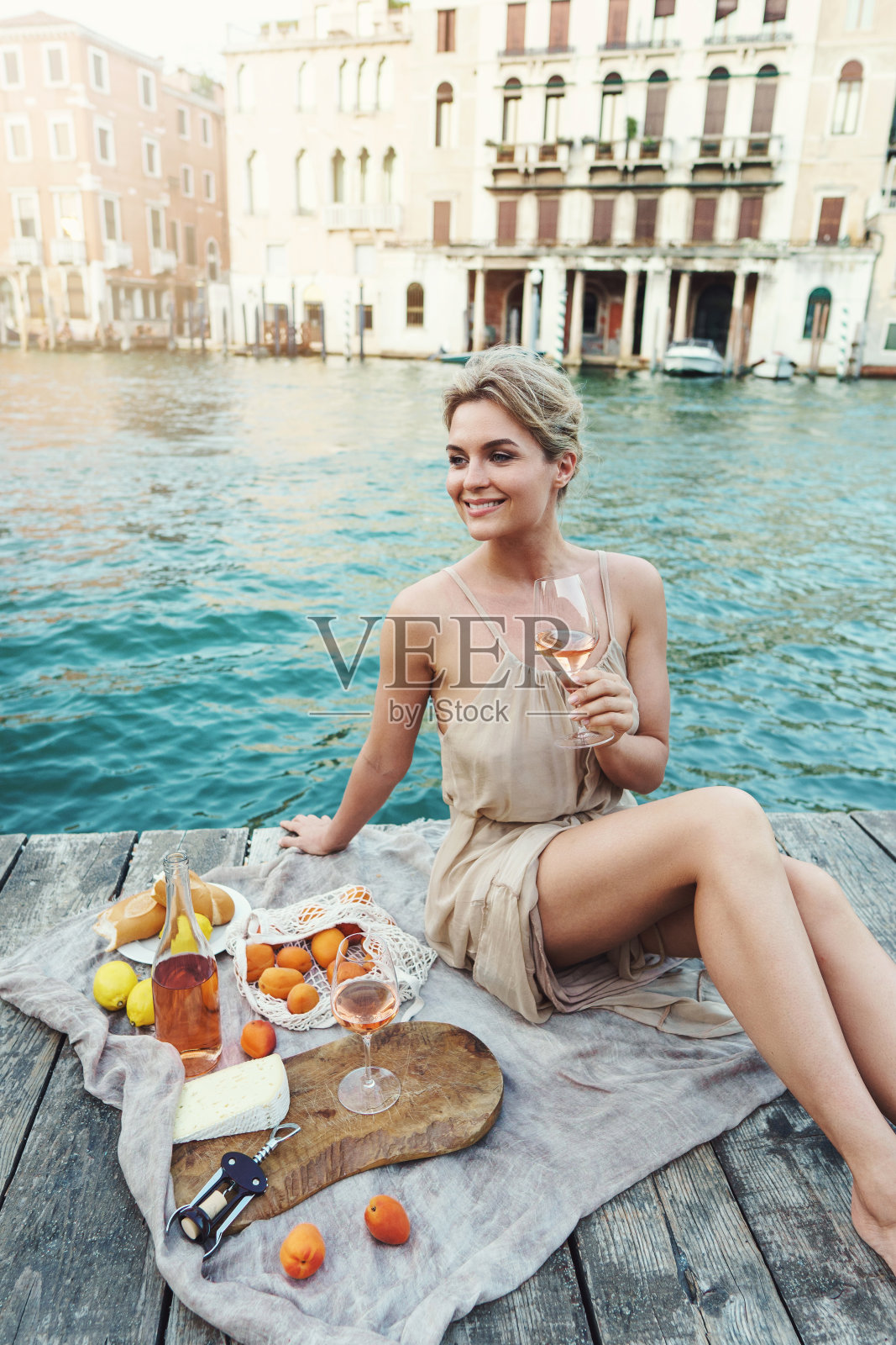 可爱的年轻女子在木制贡多拉码头上野餐，在木制码头上享用玫瑰酒、水果和小吃照片摄影图片