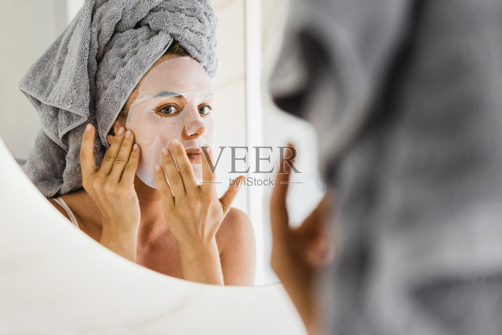 一个女人在浴室里，脸上敷着面膜，看着镜子照片摄影图片
